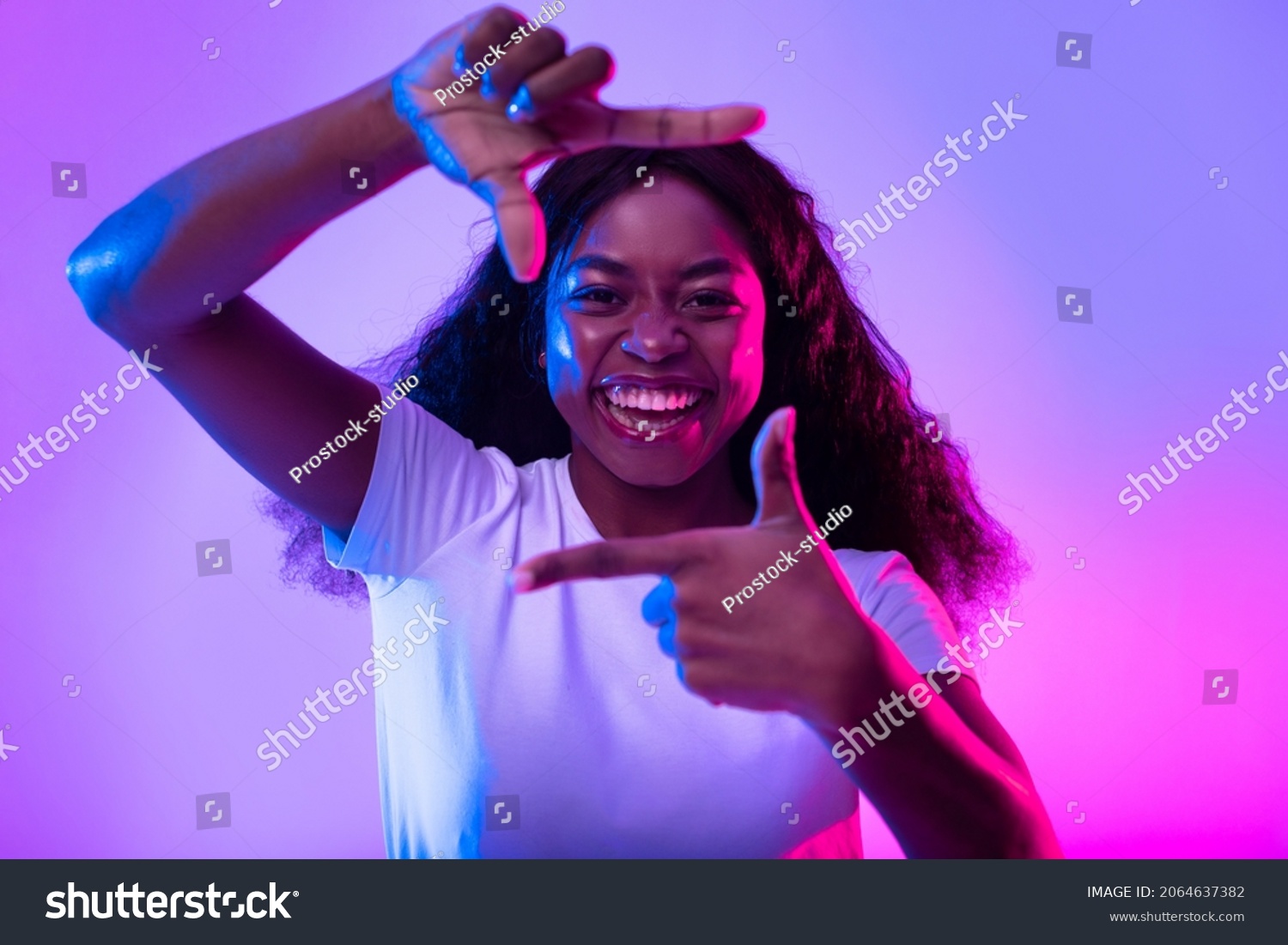 Capturing moments. Happy black woman making picture frame with fingers, looking at camera and smiling for photo in neon light. African American lady showing photograph gesture #2064637382