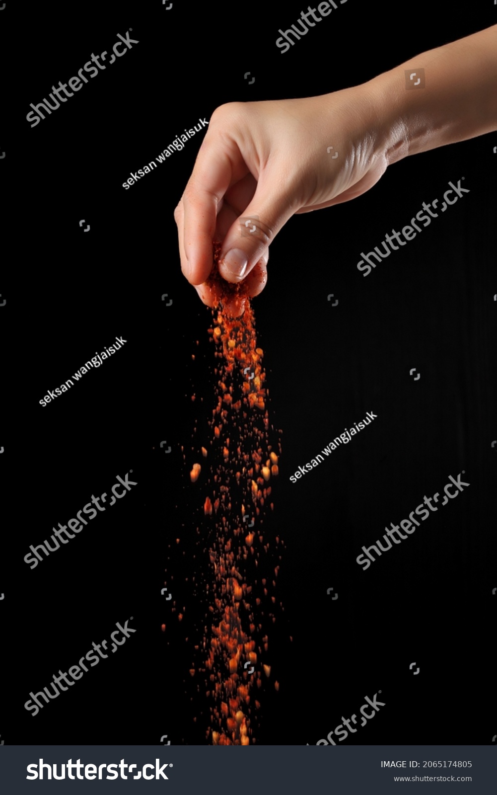 Hand sprinkling cayenne pepper isolated on black background #2065174805
