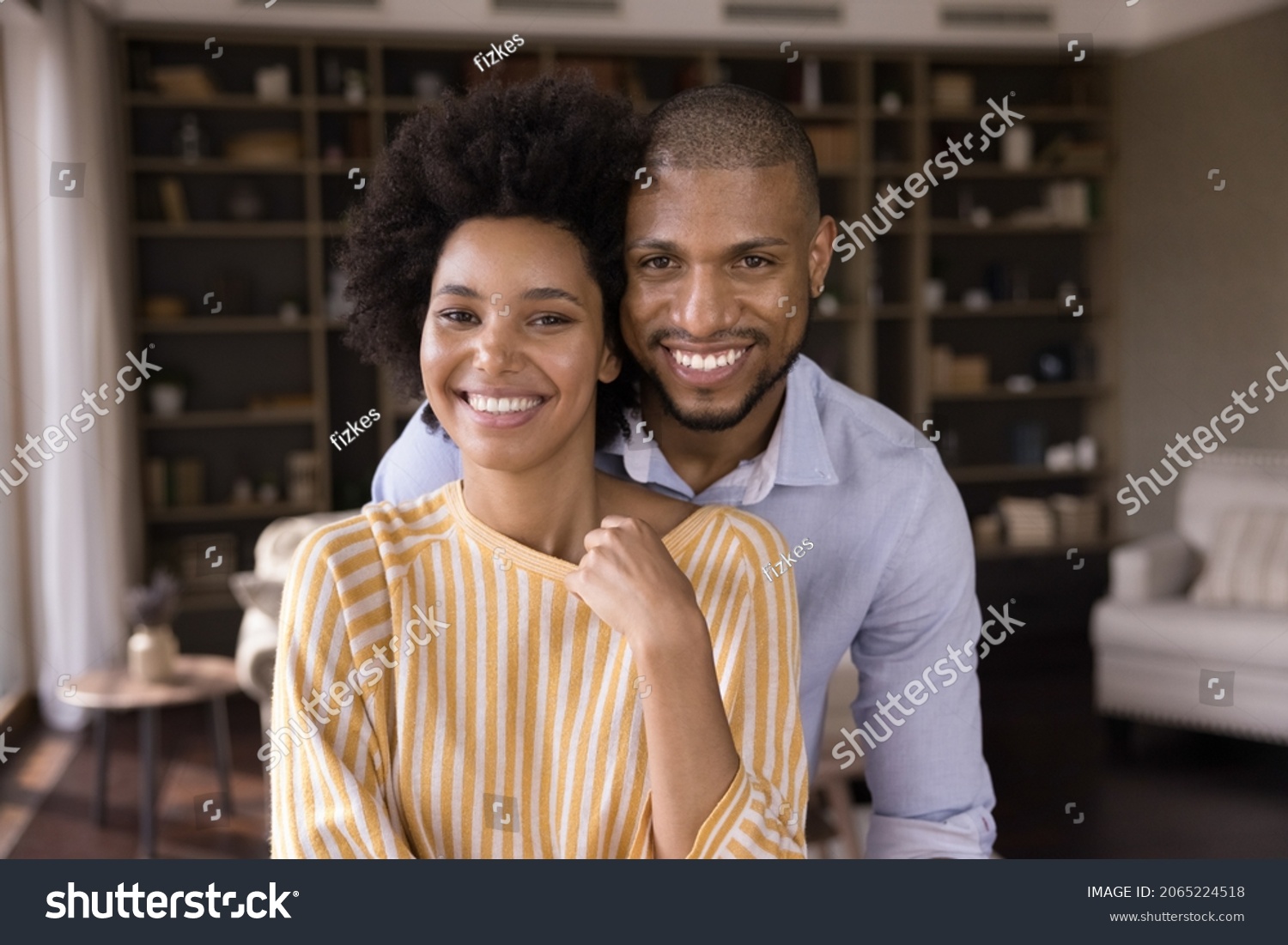 Portrait of happy loving young mixed race family couple posing in modern living room. Smiling bonding millennial homeowners celebrating moving into own apartment, good family relations concept. #2065224518