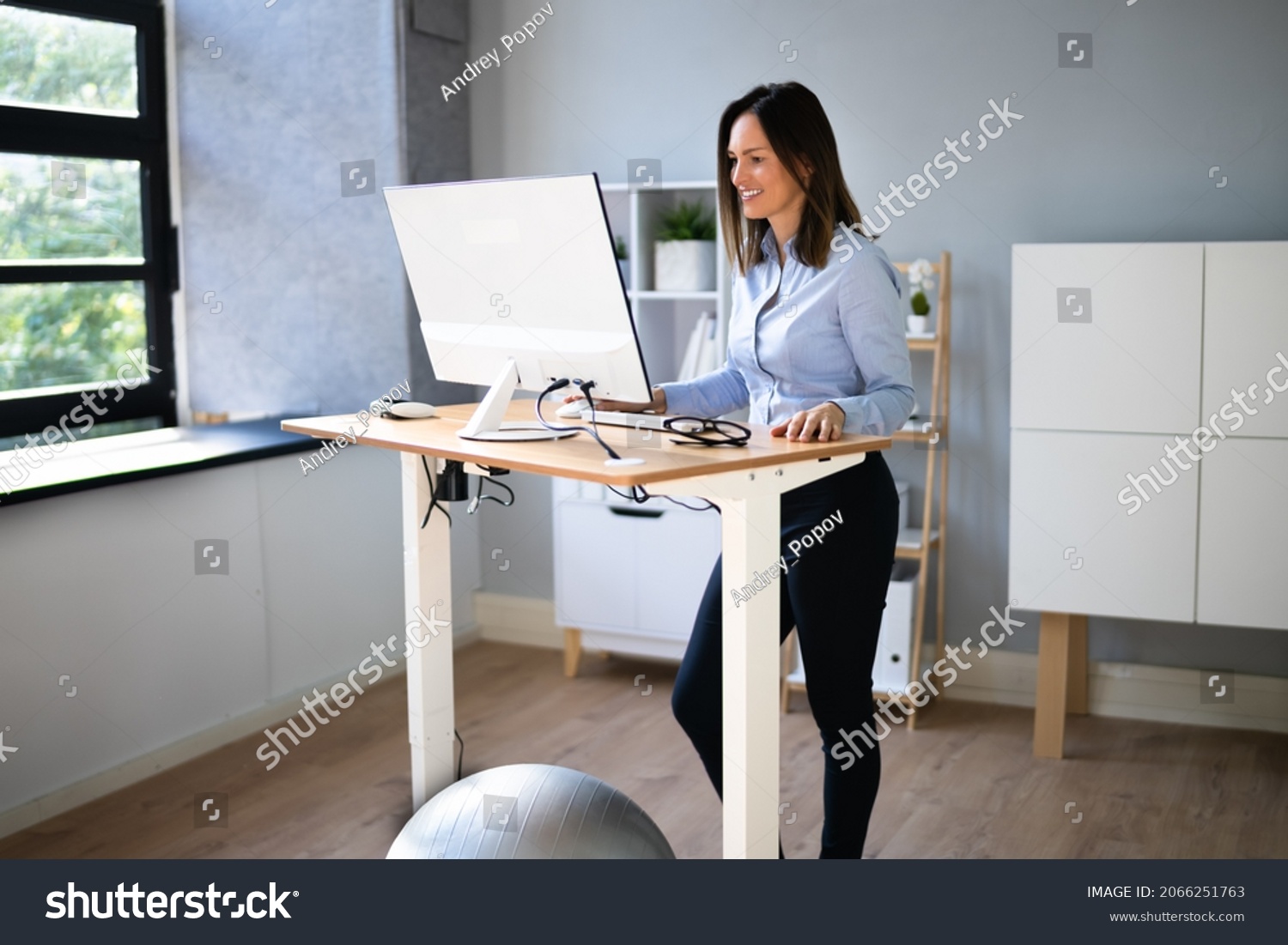 Woman Using Adjustable Height Standing Desk In Office For Good Posture #2066251763