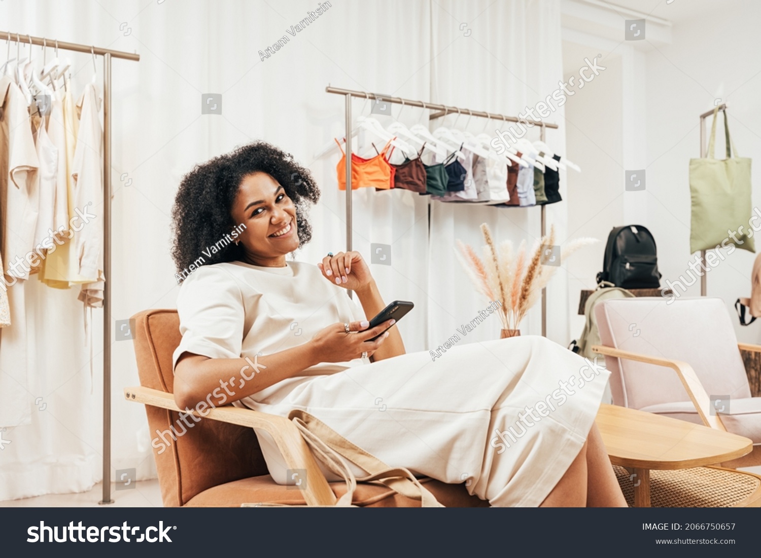 Smiling woman with mobile phone relaxing in small boutique and looking at camera #2066750657