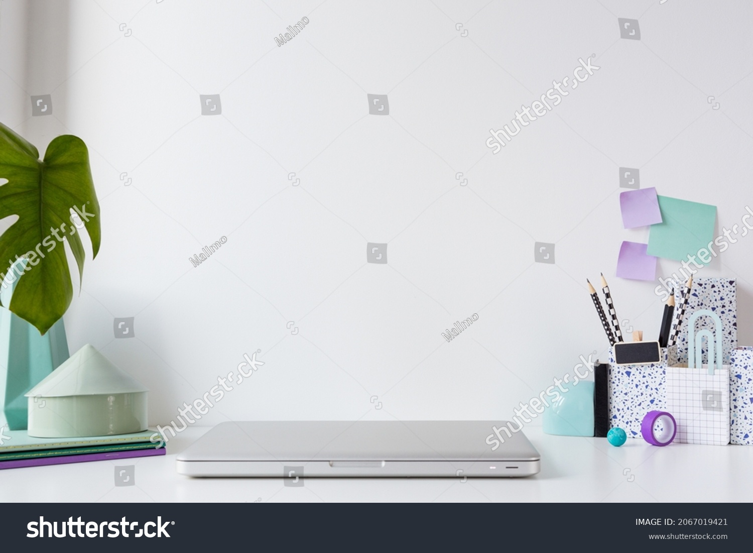 Home office. Table with closed laptop, books and supplies in purple colour. Stylish creative mock up with wall copy space. #2067019421