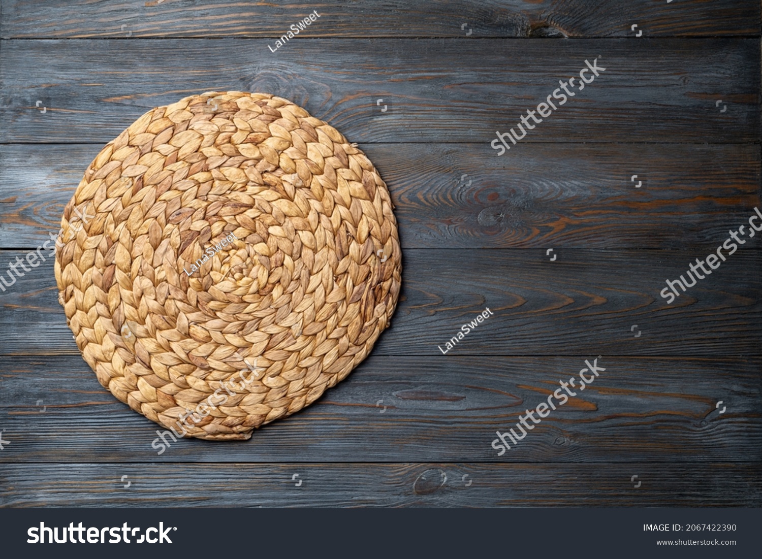 Wicker straw place mat on wooden dark background. Round woven straw mat on wooden gray dining table. Menu, dining, eating concept. Top view, copy space #2067422390