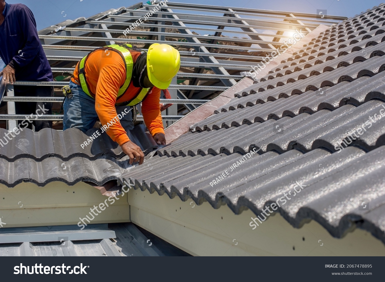 Roof repair, worker  replacing gray tiles or shingles on house with blue sky as background and copy space, Roofing - construction worker standing on a roof covering it with tiles. #2067478895