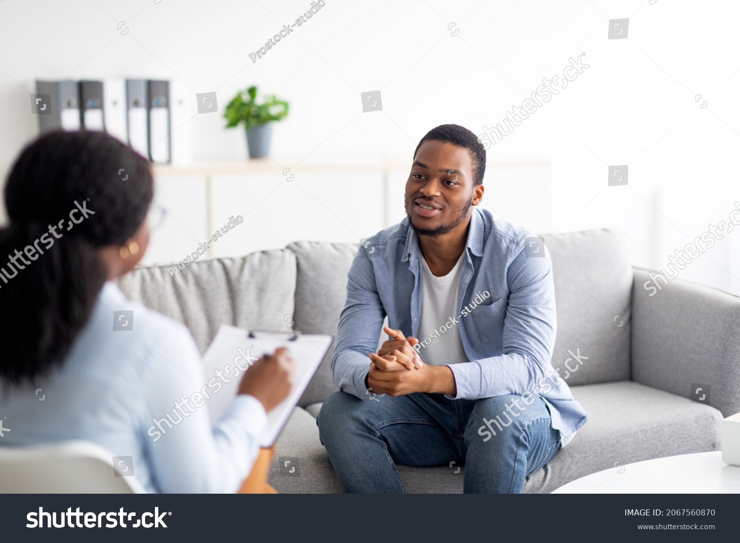 Effective psychotherapy. Young black guy talking to his psychologist, receiving professional help at mental health clinic. African American male patient sharing therapy results with counselor #2067560870