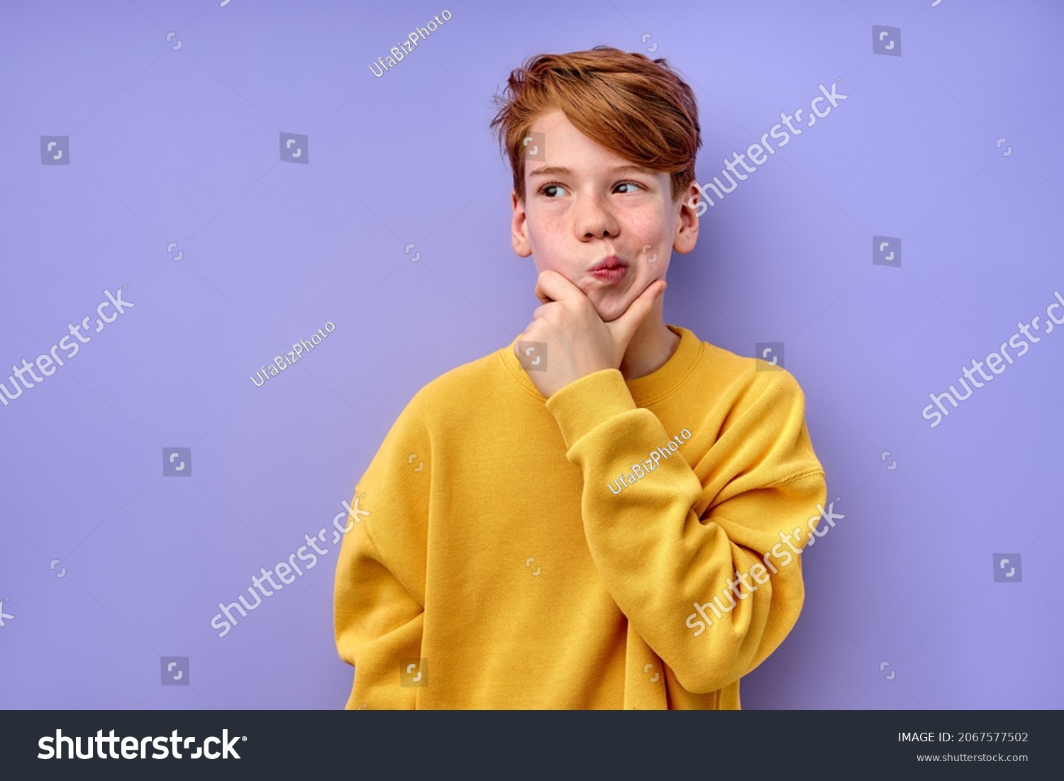 Let me think. Caucasian pensive clever redhead schooler in yellow shirt with puzzled serious expression, child thinking doubting, making choice. indoor studio shot isolated on purple background #2067577502