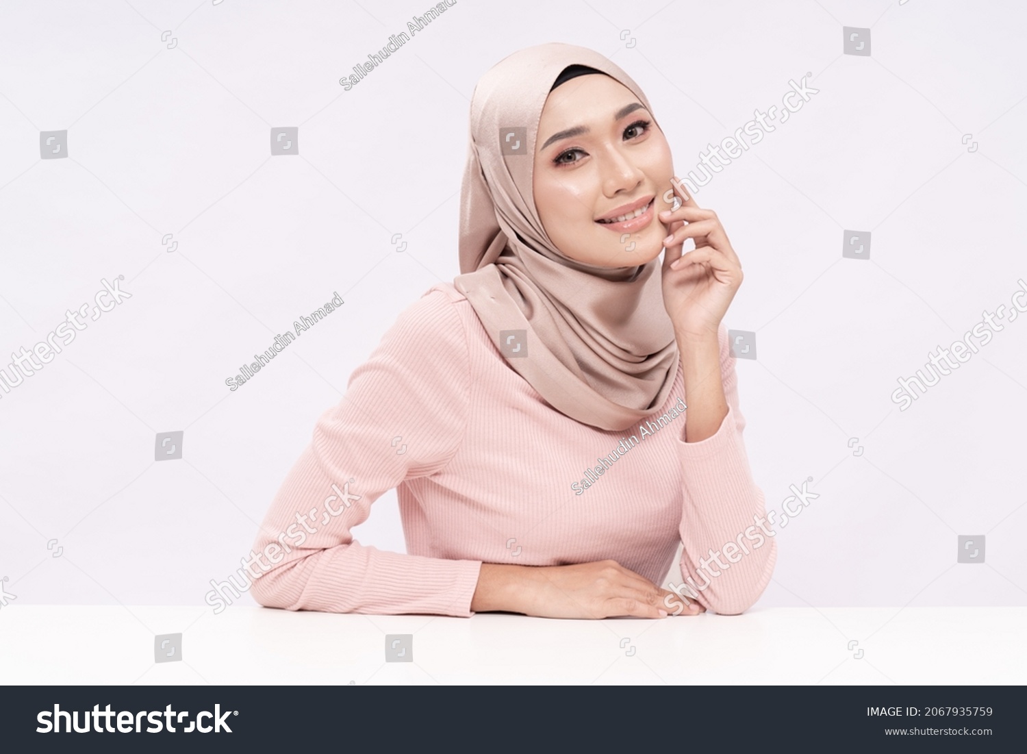 A beauty shot of a pretty young hijab girl with smooth glowing skin relaxing on a table over white background studio. Beauty skin care concept. #2067935759