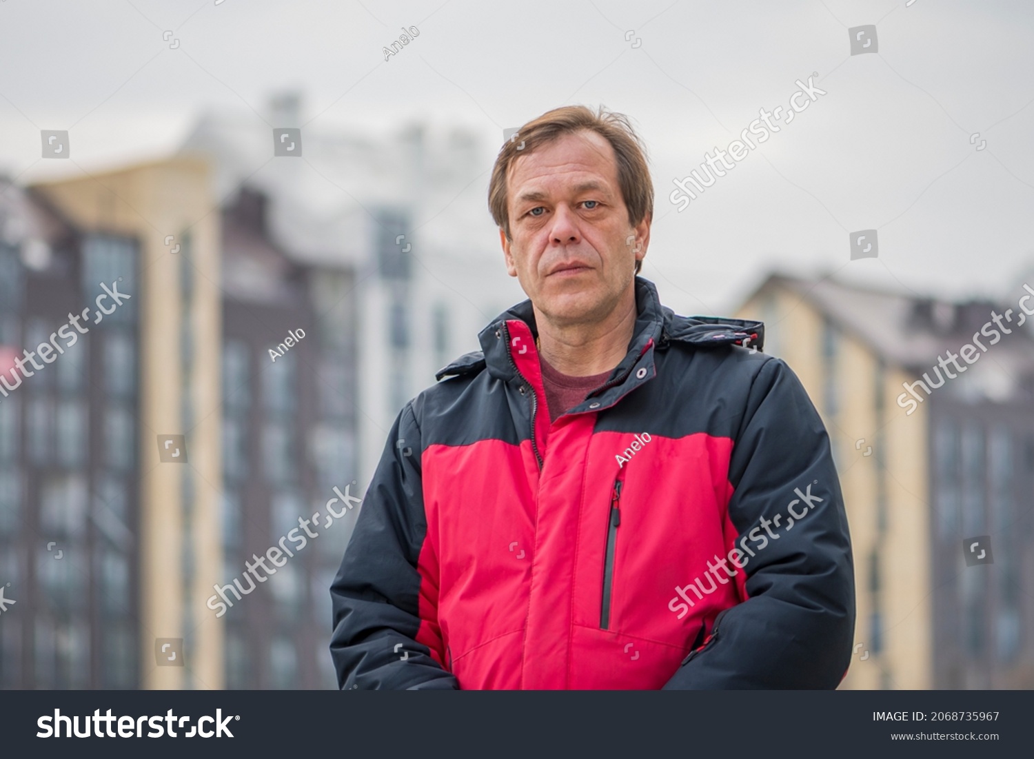 Street portrait of a 45-50-year-old man with a serious expression on the background of urban high-rise buildings, medium plan. Maybe he is a military pensioner or an actor, a truck driver, a buyer. #2068735967