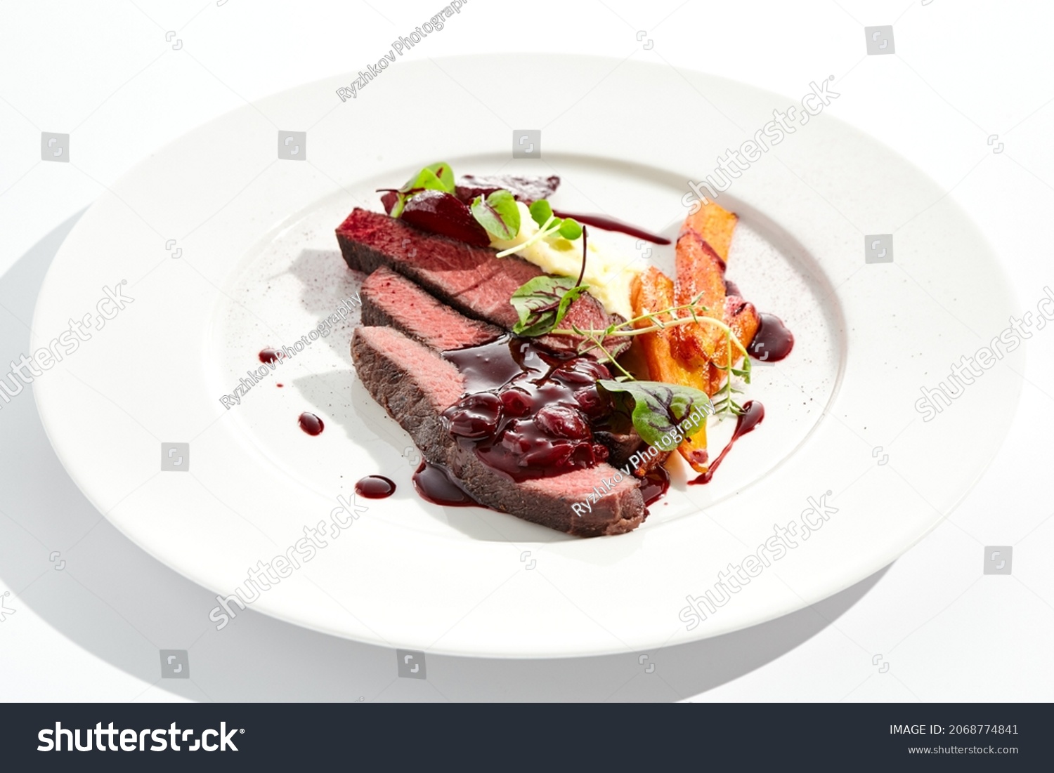 Venison steak with baked vegetables isolated on white plate. Meat steak medium rare roasted with carrot, beetroot and mashed potatoes with cherry sauce. Wild meat in restaurant menu #2068774841