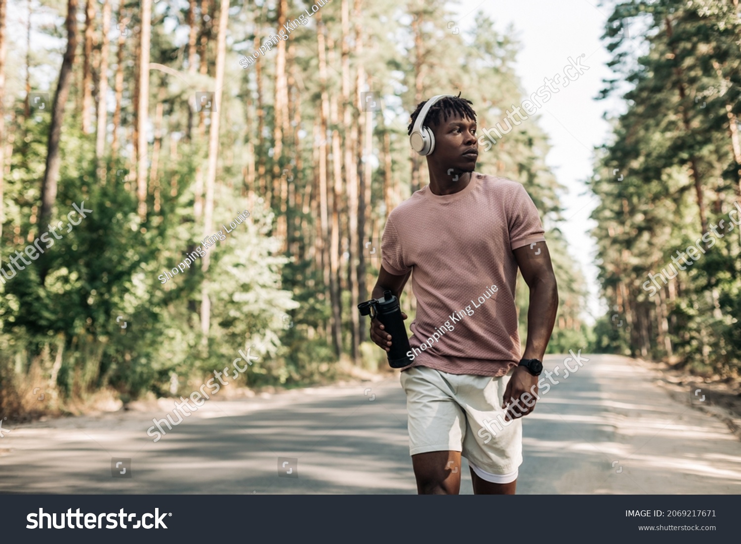 Sporty tired african american man , runner drinking water resting after workout, man relaxing after workout on city road in forest in nature #2069217671