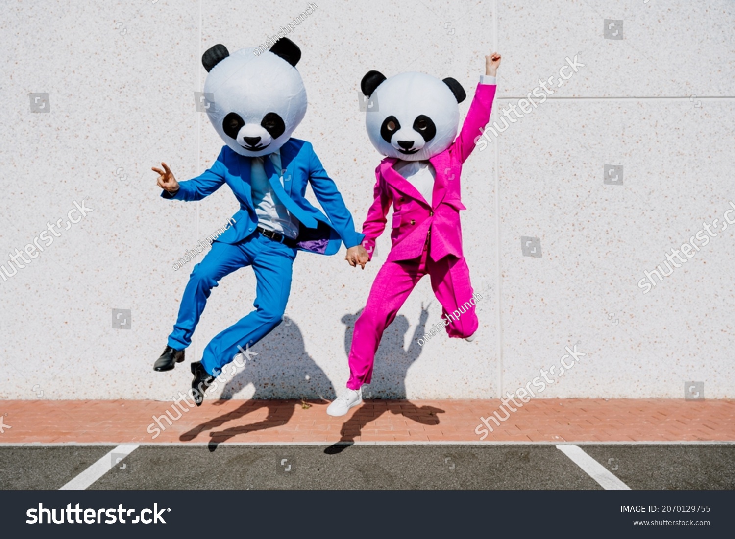 Storytelling image of a couple wearing giant panda head and colored suits. Man and woman making party in a parking lot. #2070129755
