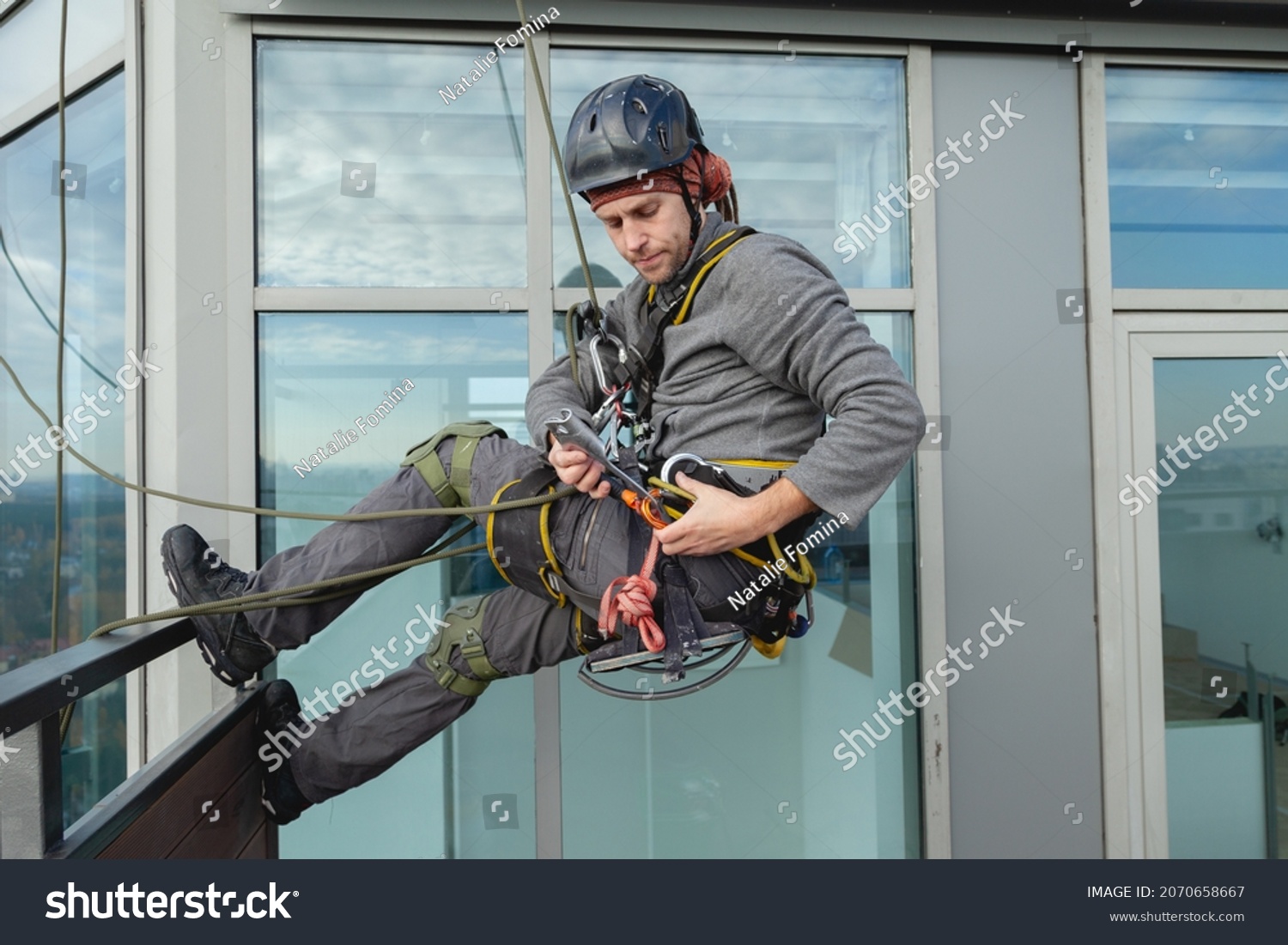 Industrial climber is preparing to hang out from the balcony of the building. Preparation for high-altitude work #2070658667