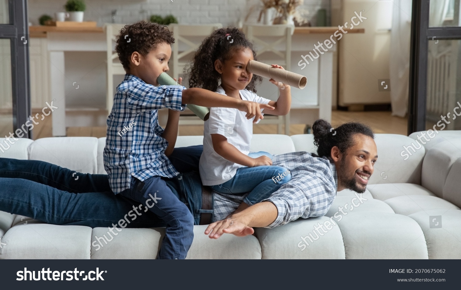 Happy African American daddy and little sibling kids playing funny active games on couch, Children sailing dad like pirate boat, holding paper toy spyglasses. Childhood, family, fatherhood #2070675062