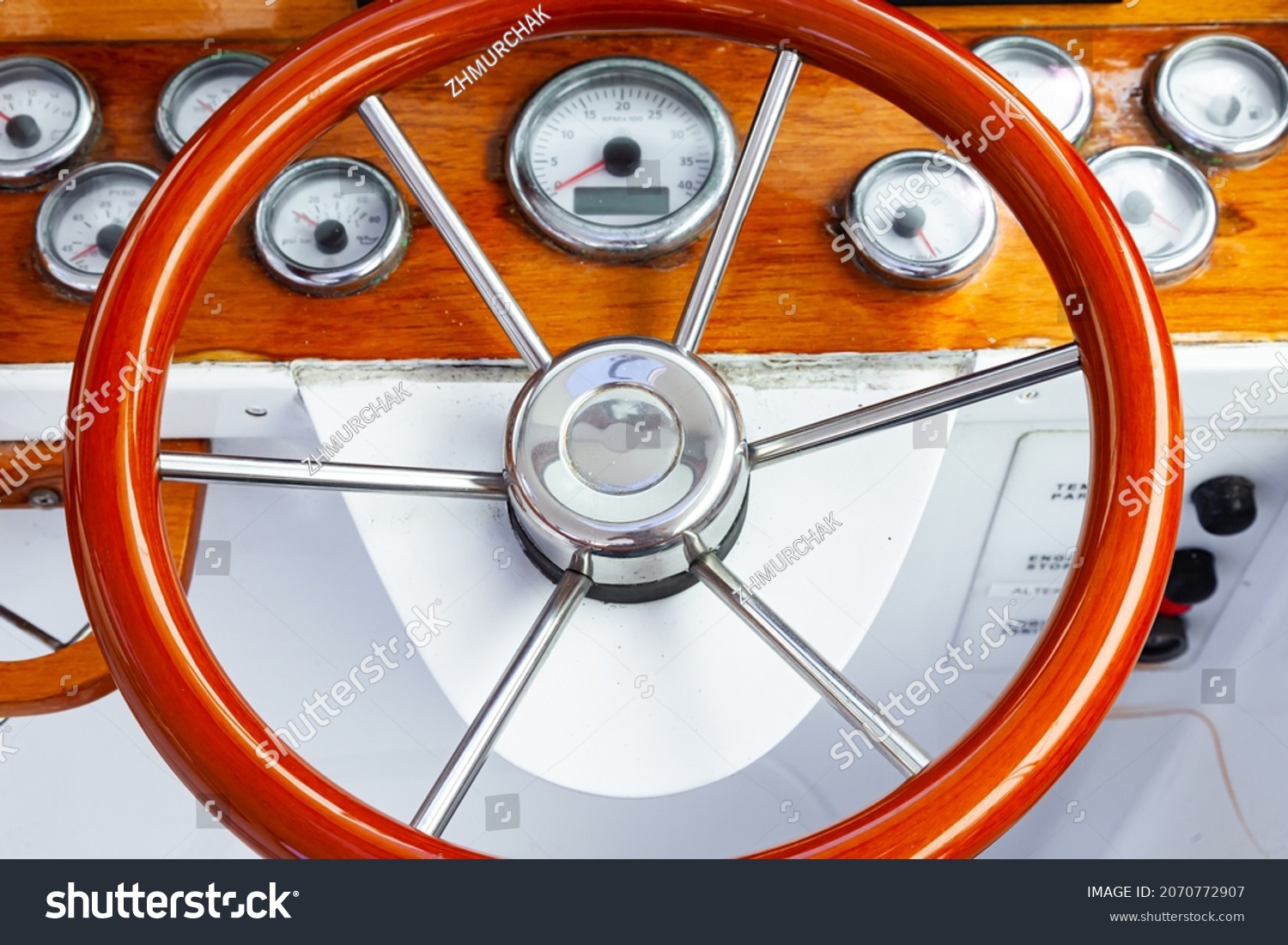 The cockpit of a luxury yacht with a classic, circular steering wheel and navigation equipment. #2070772907