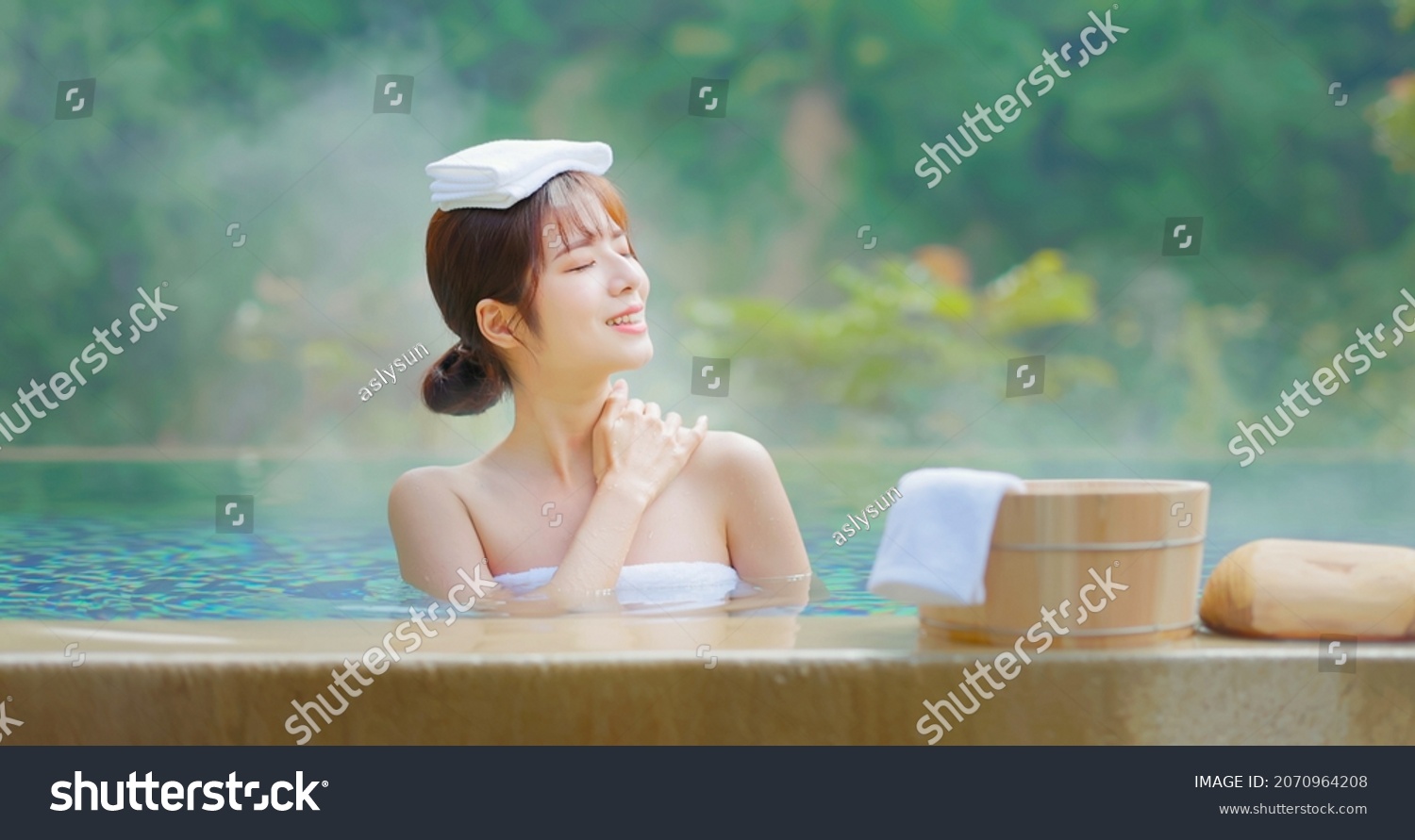 smiling asian young woman sitting on the bathtub is relaxing in hot spring with towel on head #2070964208