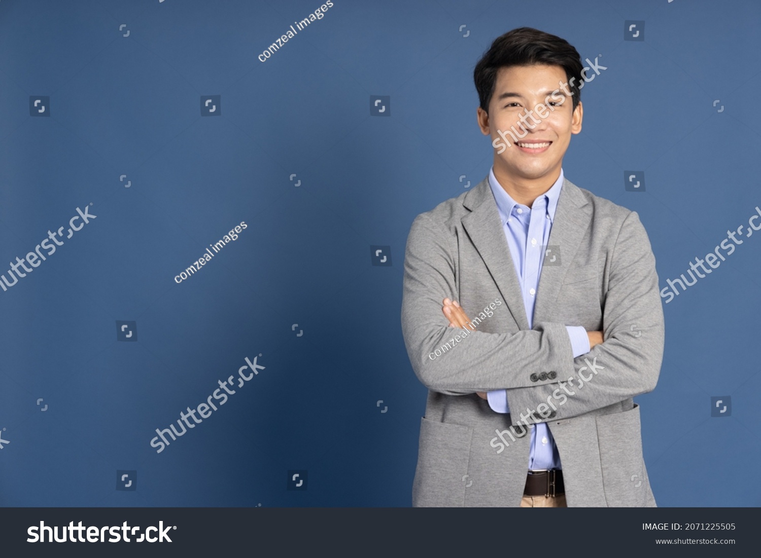 Smiling young Asian businessman with arms crossed in blue studio isolated background #2071225505