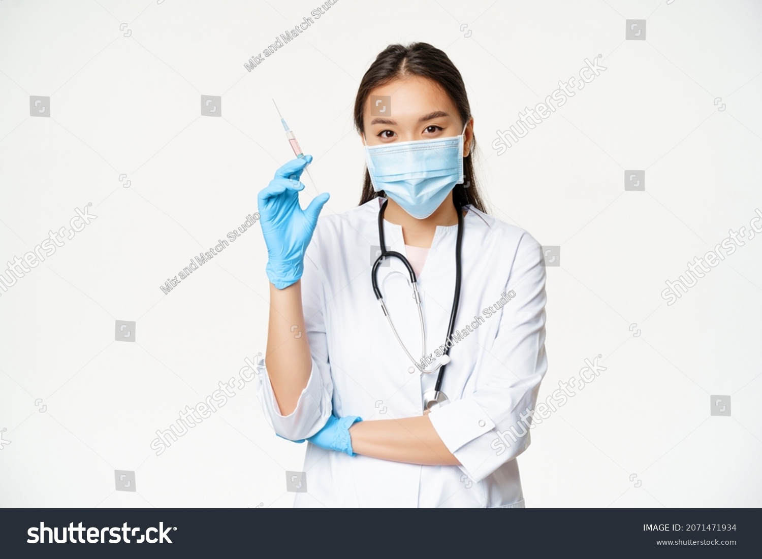 Vaccination and healthcare concept. Asian female doctor, nurse in medical face mask and gloves holding syringe with vaccine, white background #2071471934