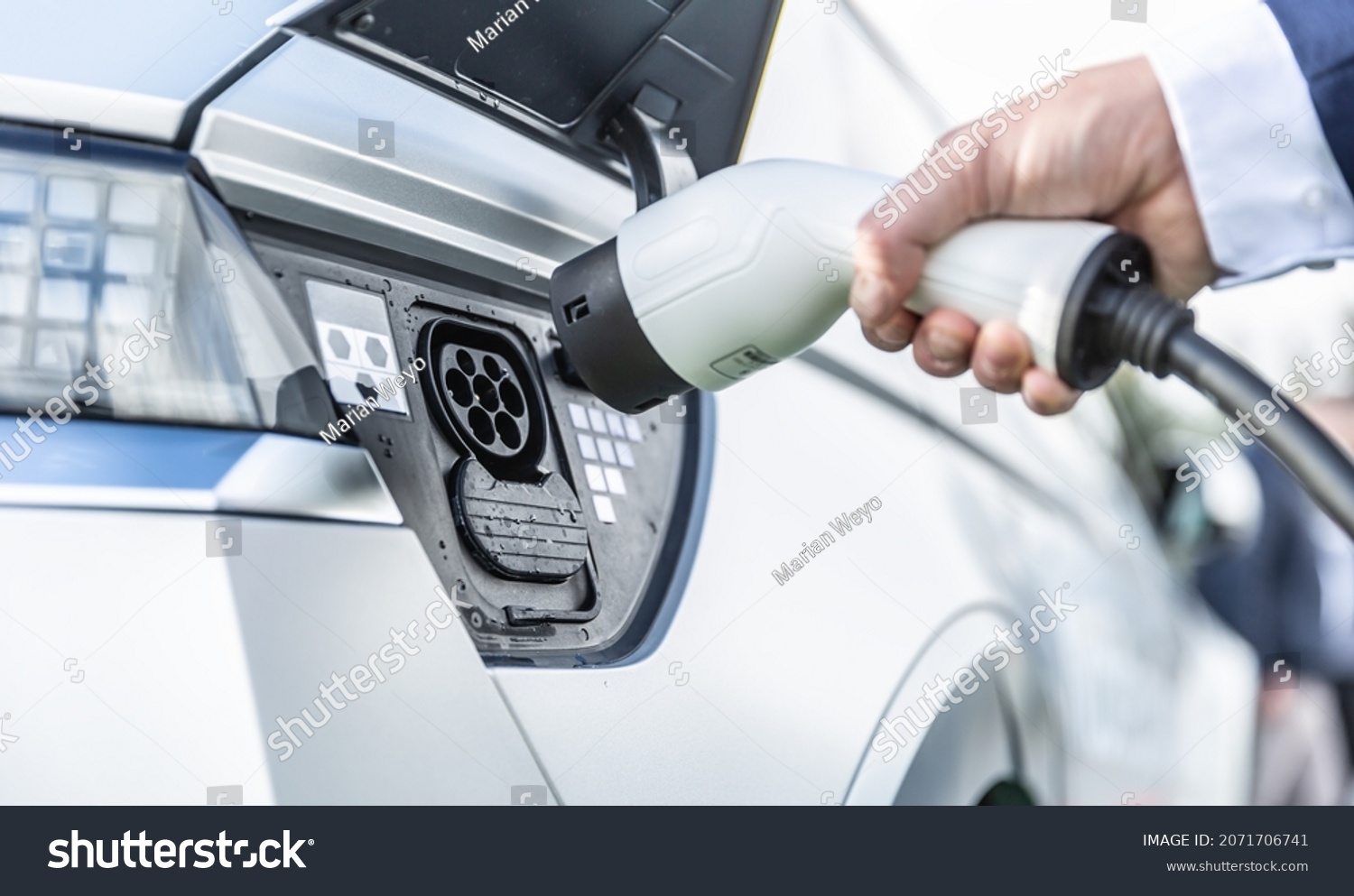 The driver of the electric car inserts the electrical connector to charge the batteries. #2071706741