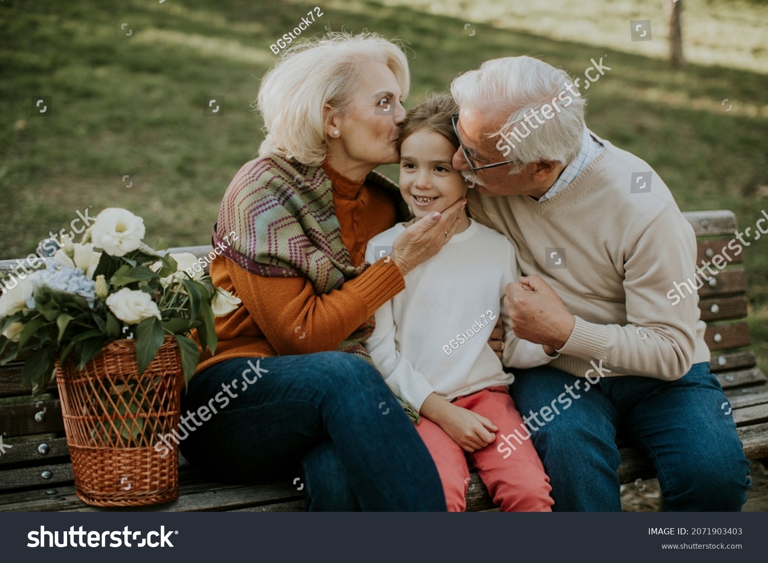 Heathy senior couple sitting on the bench witht heir cute little granddaughter #2071903403