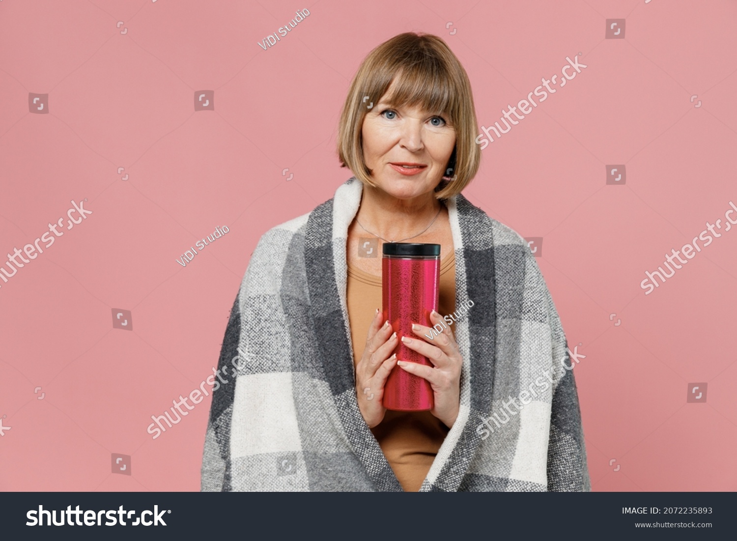 Smiling blithesome charismatic vivid fun mature elderly senior lady woman 55 years old wears motley plaid hold thermos trying to warm up isolated on plain pastel light pink background studio portrait #2072235893