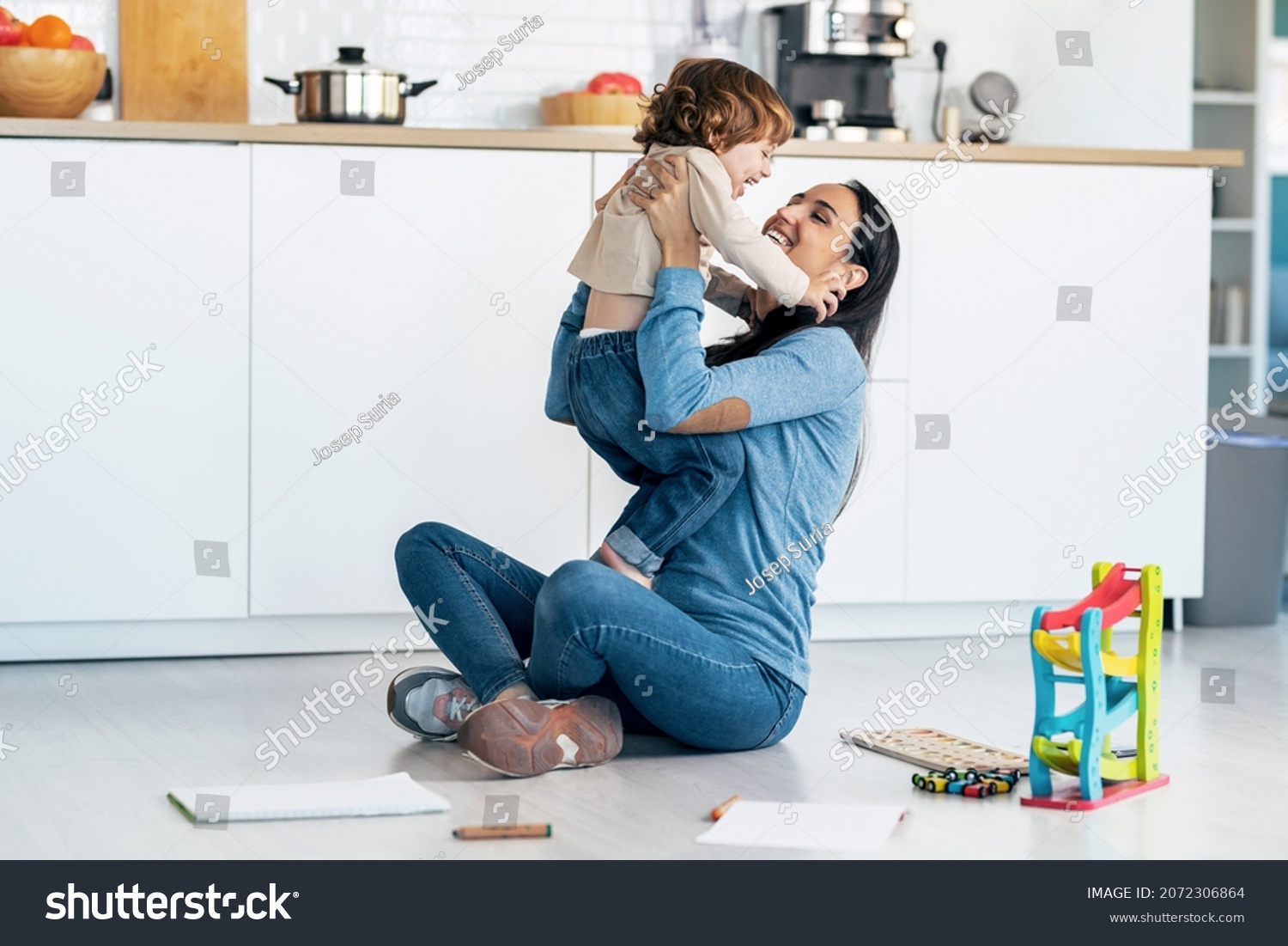 Shot of young beautiful mother playing and having fun on the floor with her son in living room at home. #2072306864