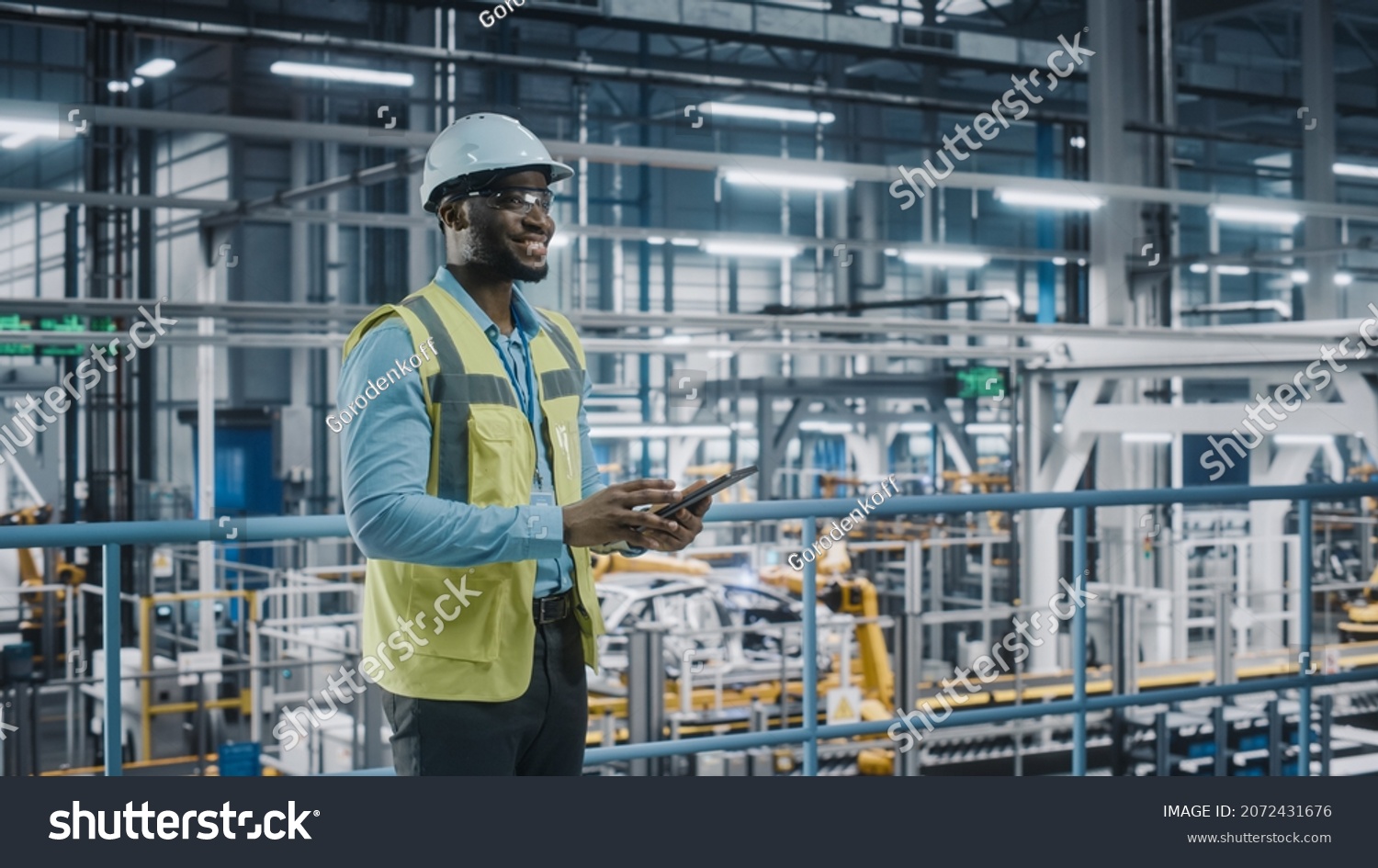 Happy African American Car Factory Engineer in High Visibility Vest Using Tablet Computer. Automotive Industrial Facility Working on Vehicle Production on Automated Technology Assembly Plant. #2072431676