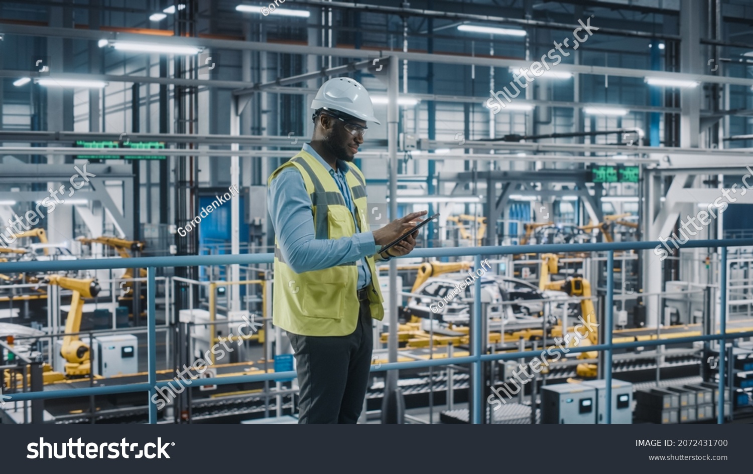 Happy African American Car Factory Engineer in High Visibility Vest Using Tablet Computer. Automotive Industrial Facility Working on Vehicle Production on Automated Technology Assembly Plant. #2072431700