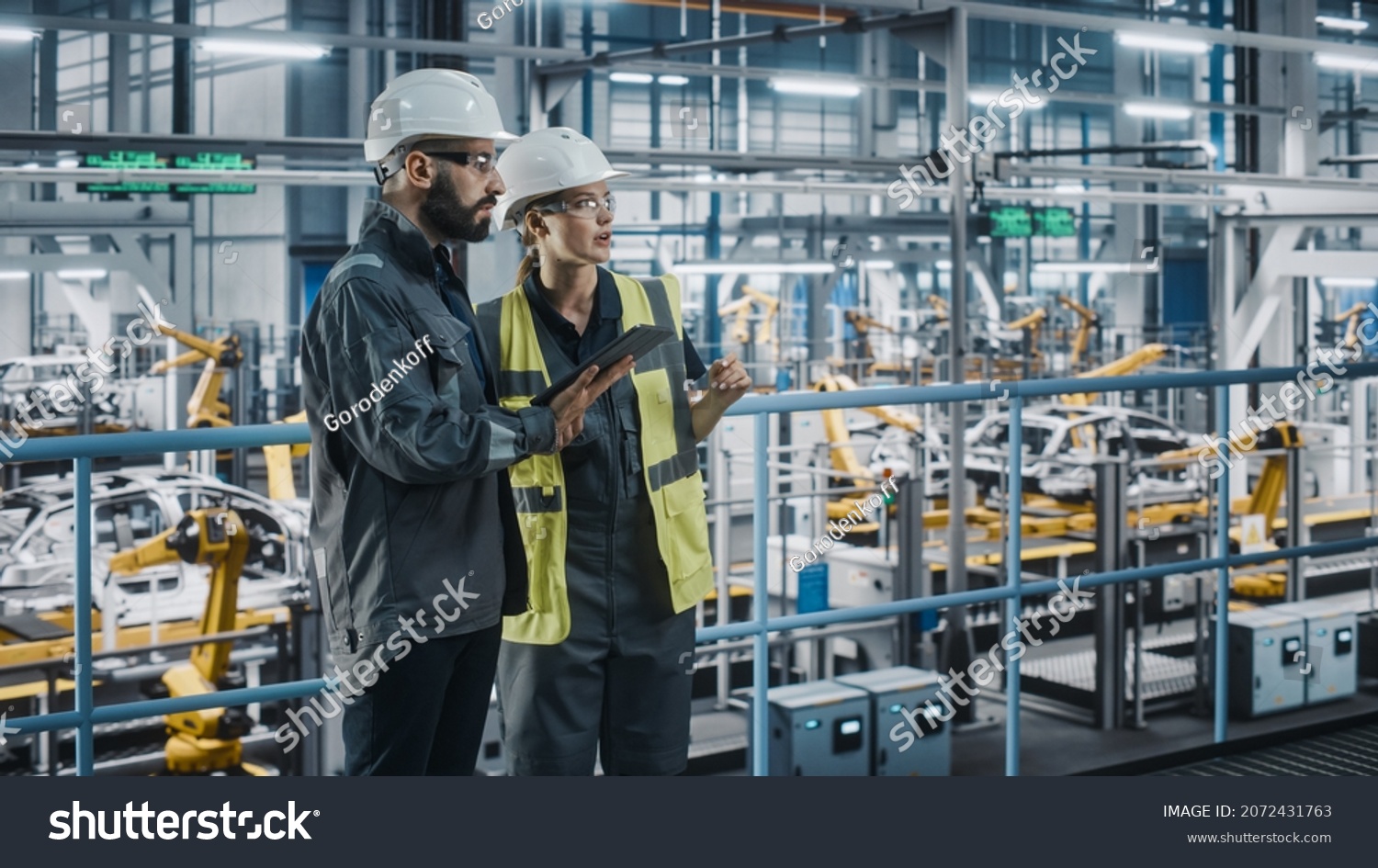 Male Specialist and Female Car Factory Engineer in High Visibility Vests Using Tablet Computer. Automotive Industrial Manufacturing Facility Working on Vehicle Production. Diversity on Assembly Plant. #2072431763