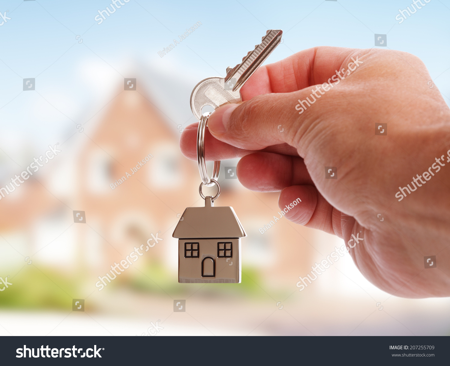 Holding house keys on house shaped keychain in front of a new home #207255709