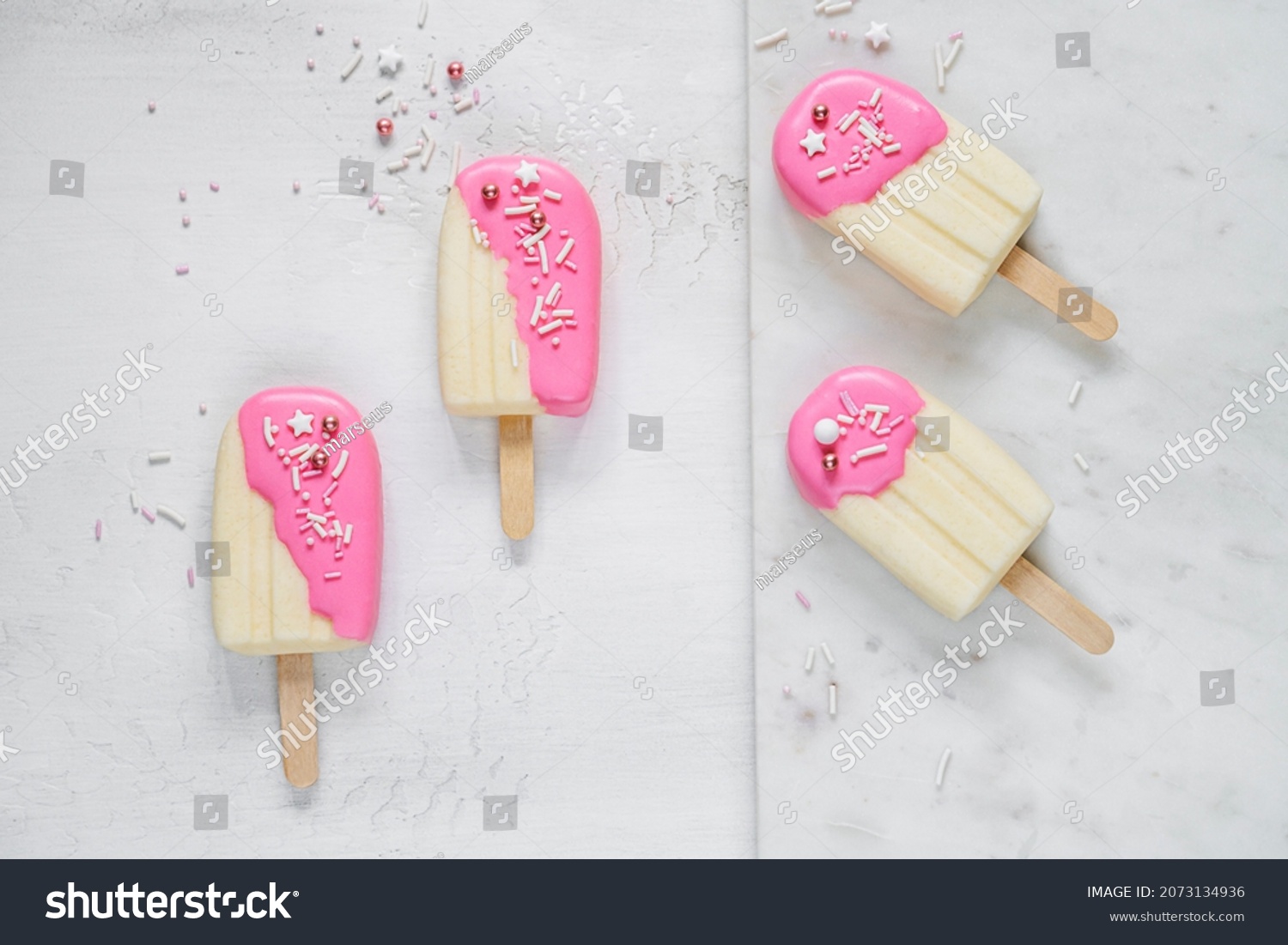 Top table view on four delicious vanilla ice cream bars with pink glaze surrounded by scattered sugar sprinkles on light background. Frozen dessert and summer snack concept #2073134936