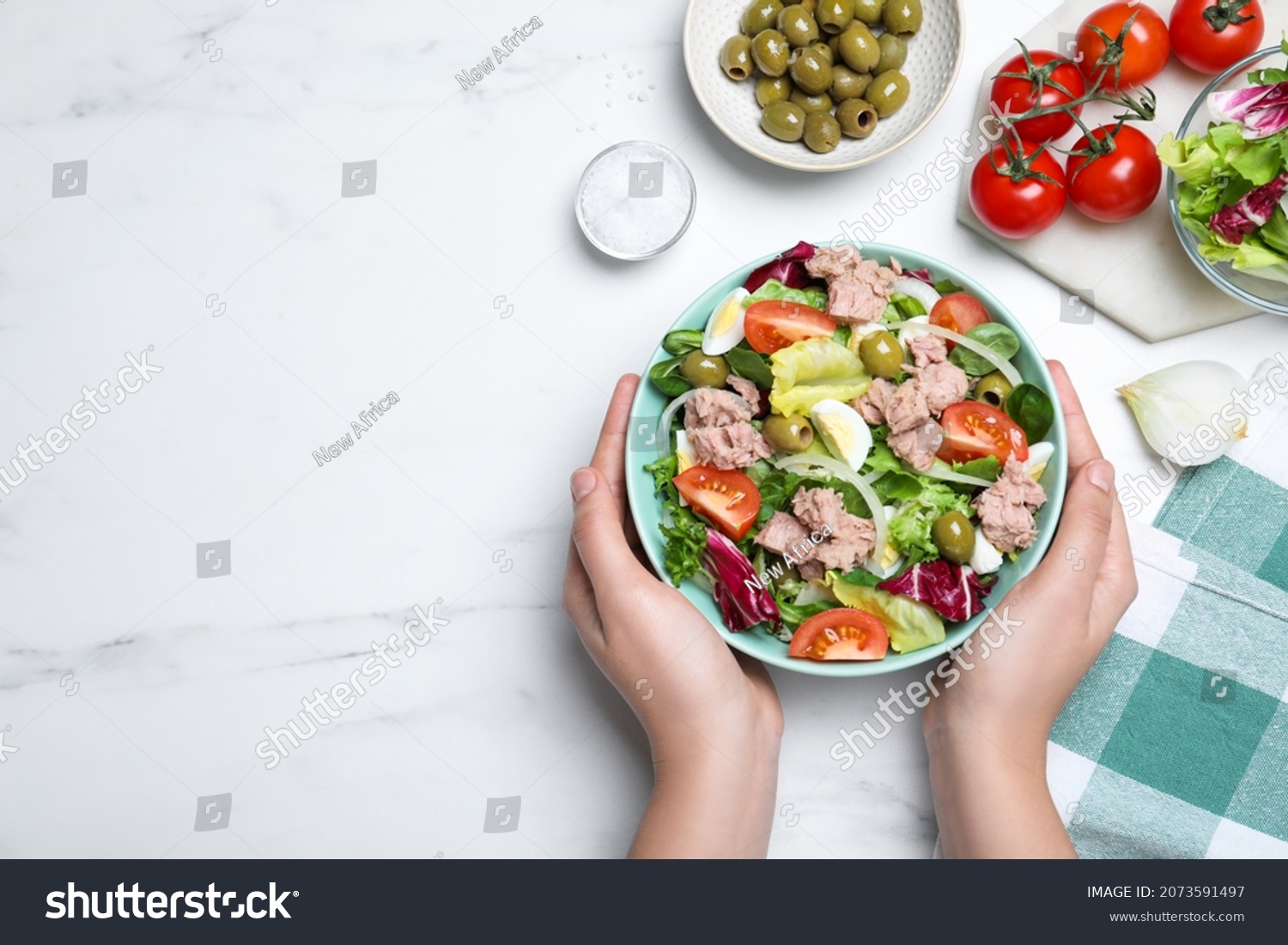 Woman holding bowl of delicious salad with canned tuna at white table, top view. Space for text #2073591497