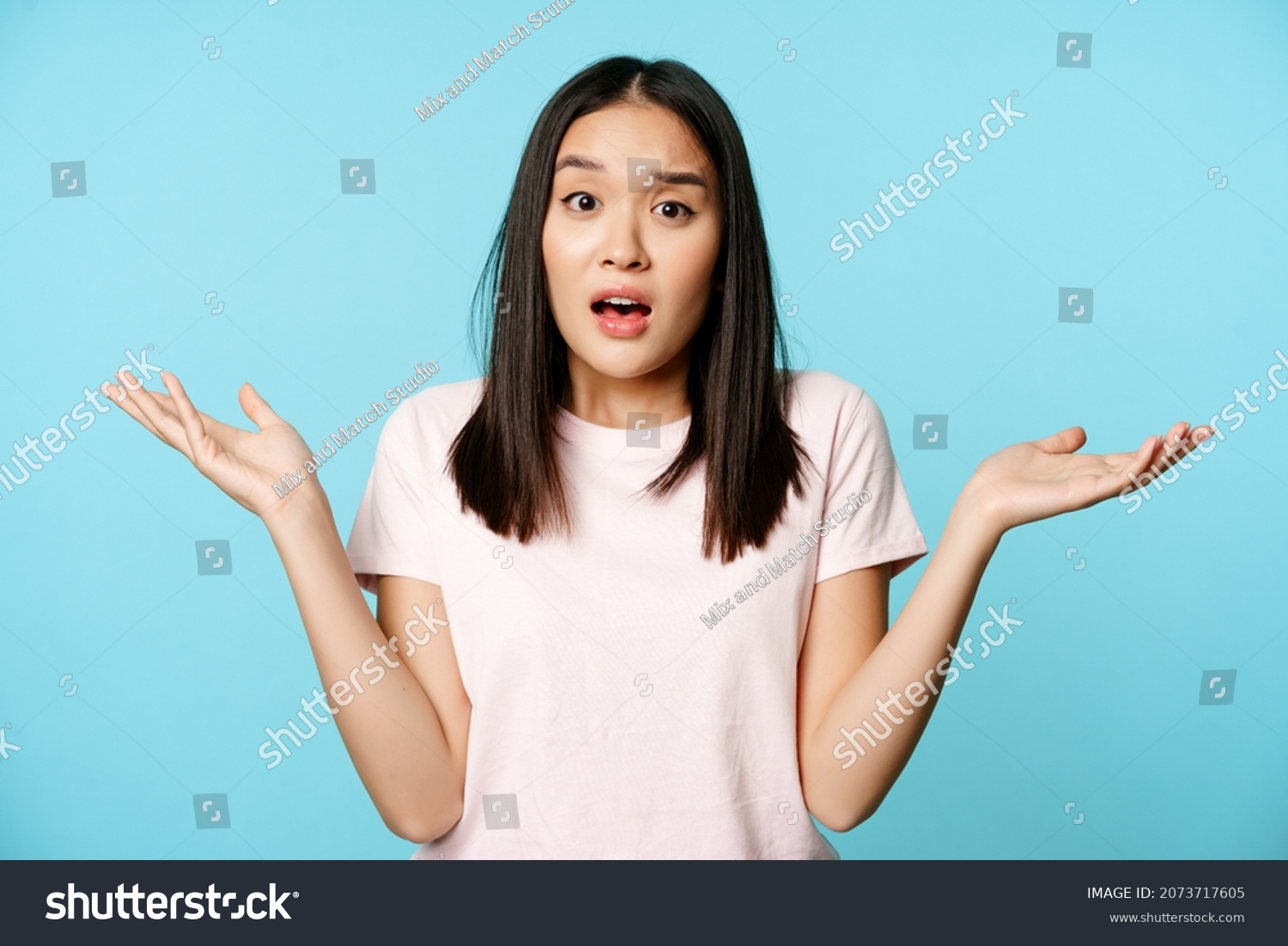 Confused asian girl spread empty hands sideways, shrugging shoulders clueless, standing in tshirt over blue background #2073717605