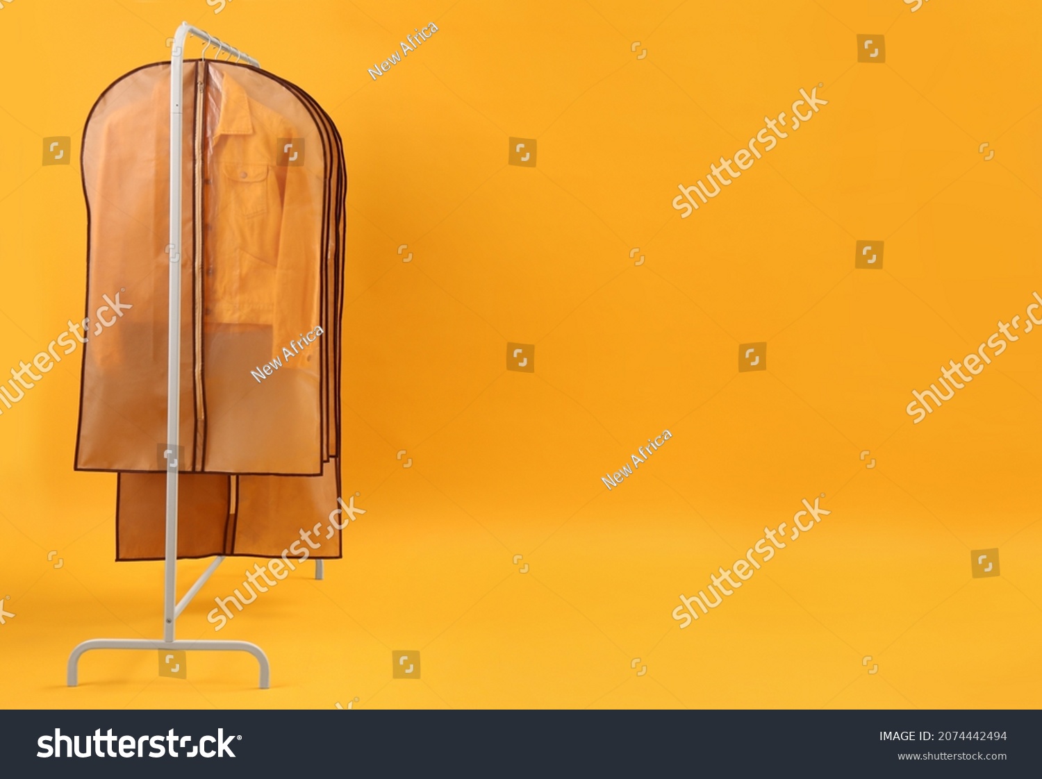 Garment bags with clothes on rack against yellow background. Space for text #2074442494
