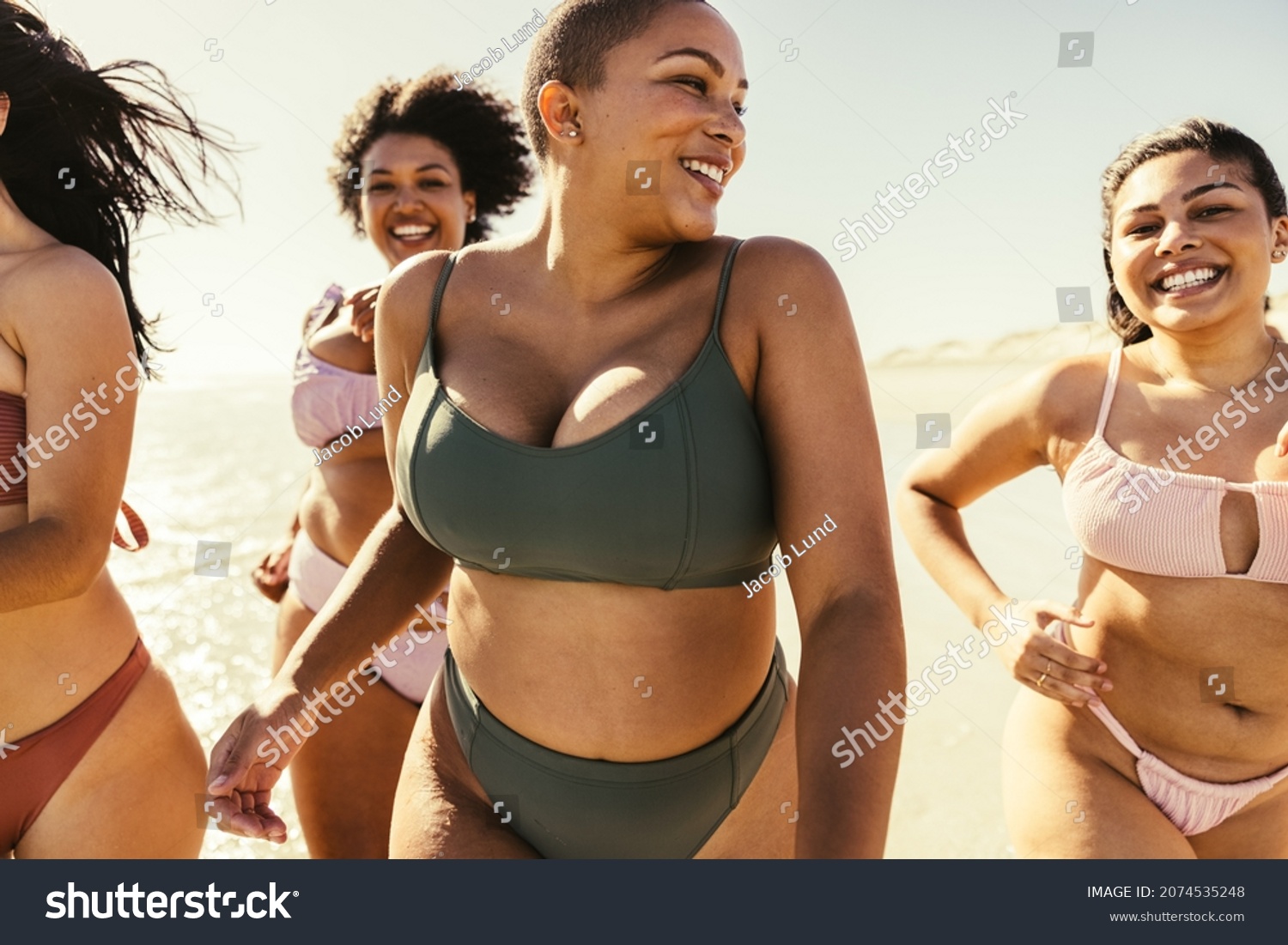 Women running in bikinis at the beach. Group of carefree young women smiling cheerfully while running in the sun. Happy female friends having fun and enjoying their summer vacation. #2074535248