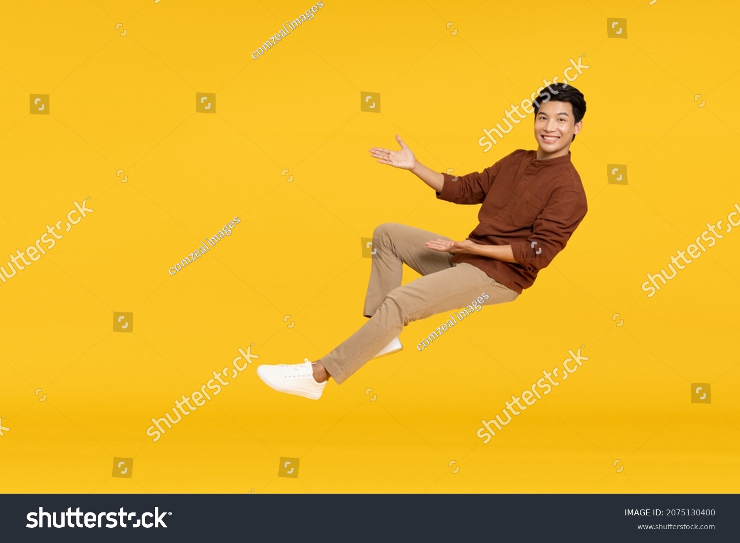 Happy cheerful young Asian man floating in the air isolated on yellow background, Presentation concept #2075130400