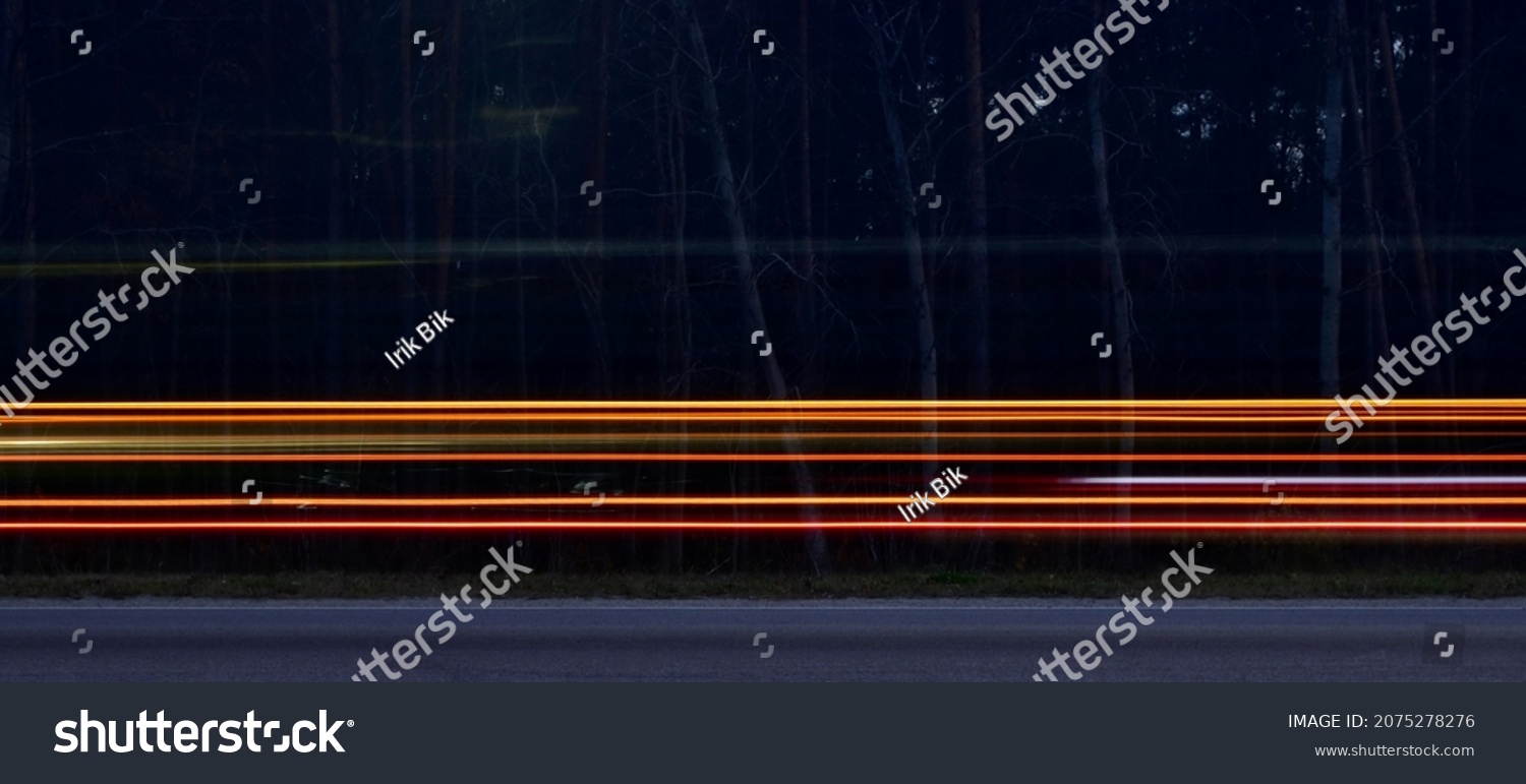 Car running lights in blurred motion on highway against dark blurred forest background #2075278276