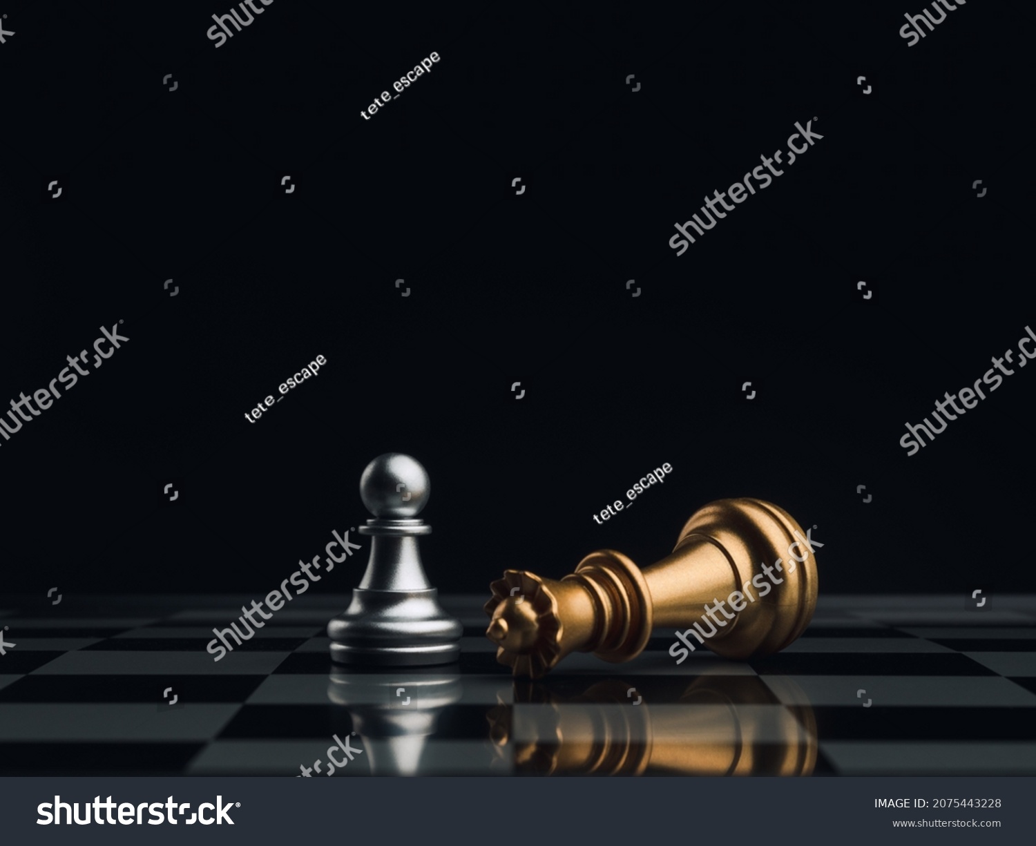A little silver pawn chess piece standing with the win near a fallen golden queen chess piece on a chessboard on dark background. Leadership, winner, brave, competition, and business strategy concept. #2075443228
