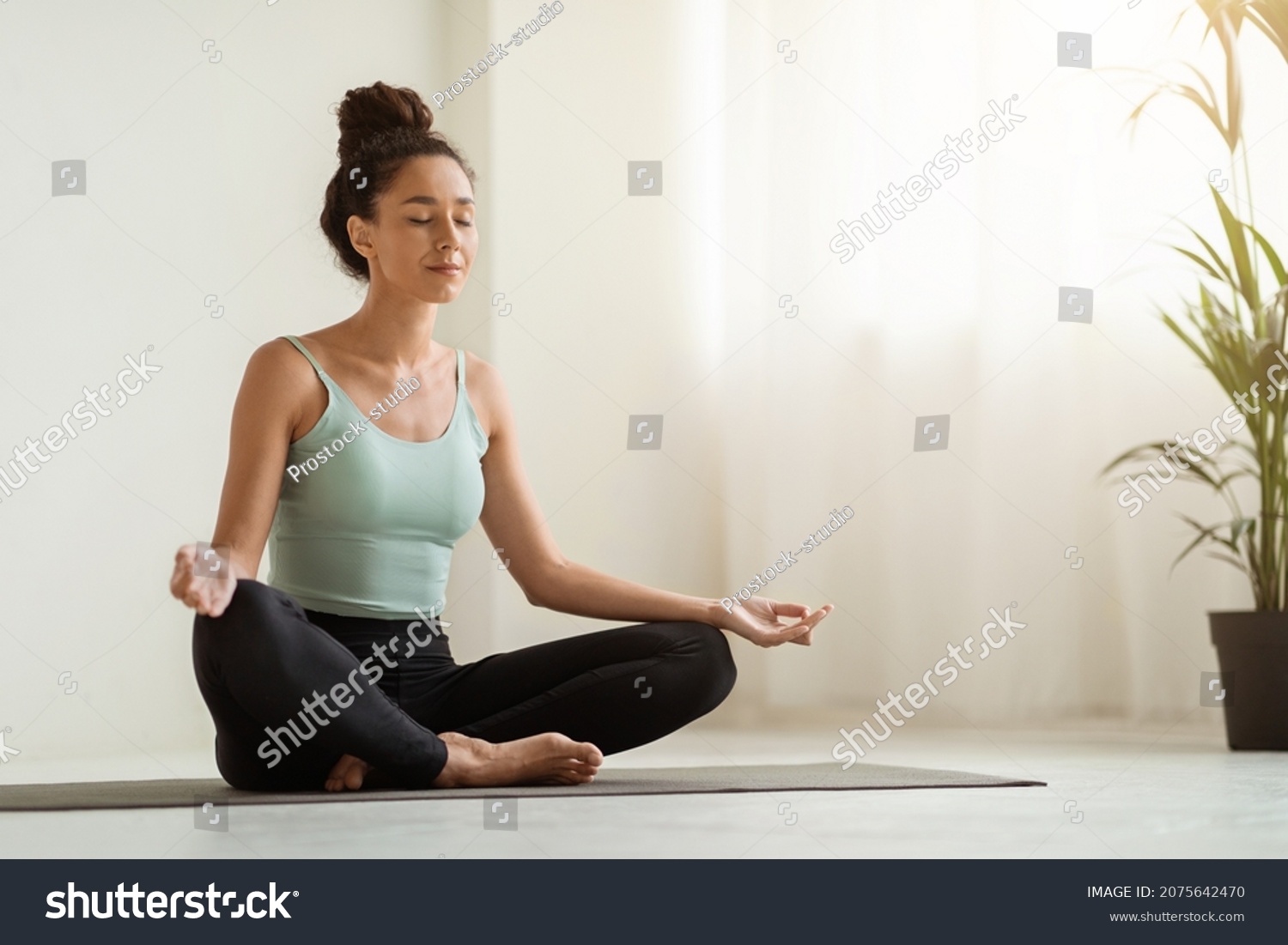 Morning Meditation. Beautiful Calm Woman Meditating At Home In Lotus Position, Peaceful Young Brunette Lady Practicing Yoga, Sitting With Closed Eyes On Fitness Mat In Light Room, Copy Space #2075642470