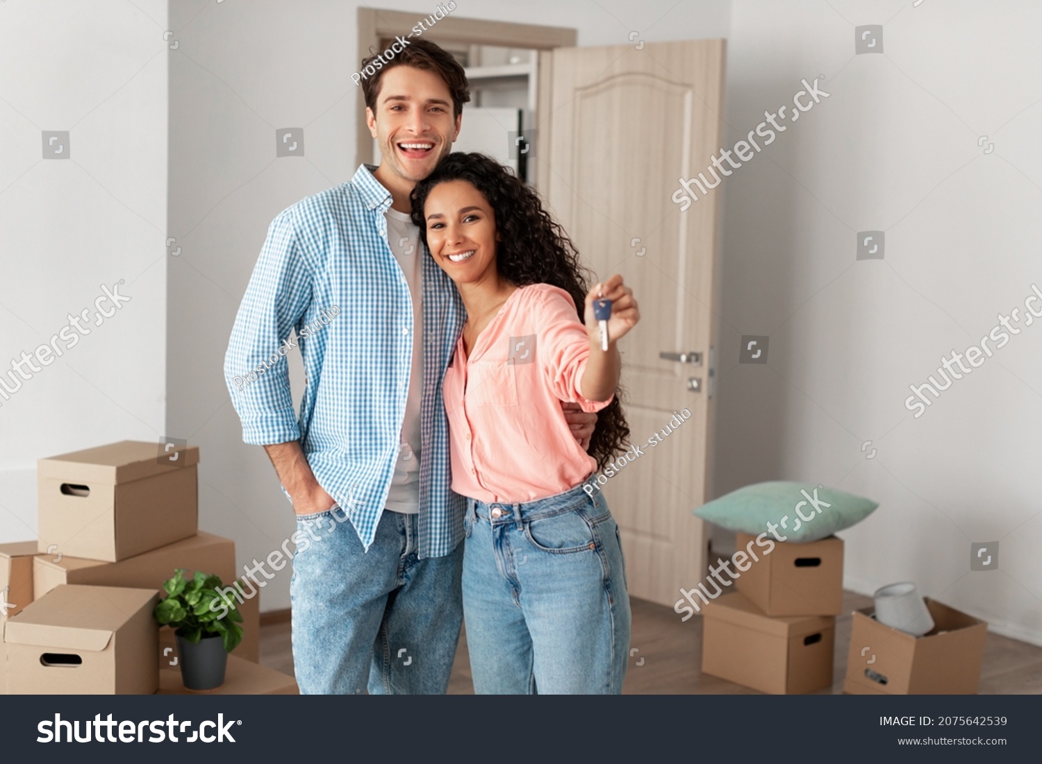 Mortgage and Relocation Concept. Portrait of happy woman hugging man, holding key from new first house, young family celebrating moving day, satisfied customers buyers couple purchase real estate #2075642539