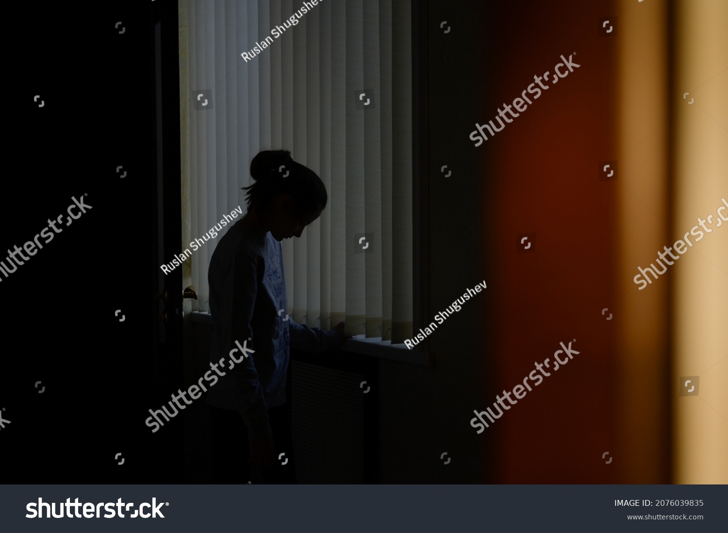 trouble and problem concept of domestic violence upset sad little girl on blue window background in sunset home room #2076039835