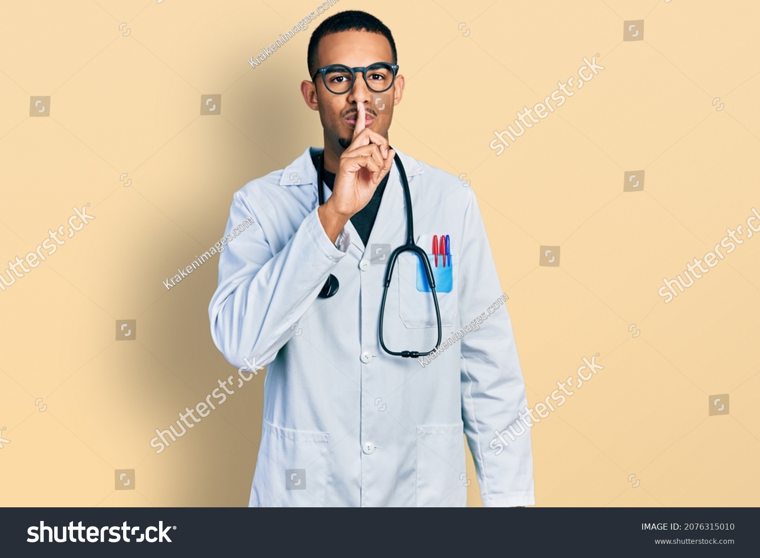 Young african american man wearing doctor uniform and stethoscope asking to be quiet with finger on lips. silence and secret concept.  #2076315010