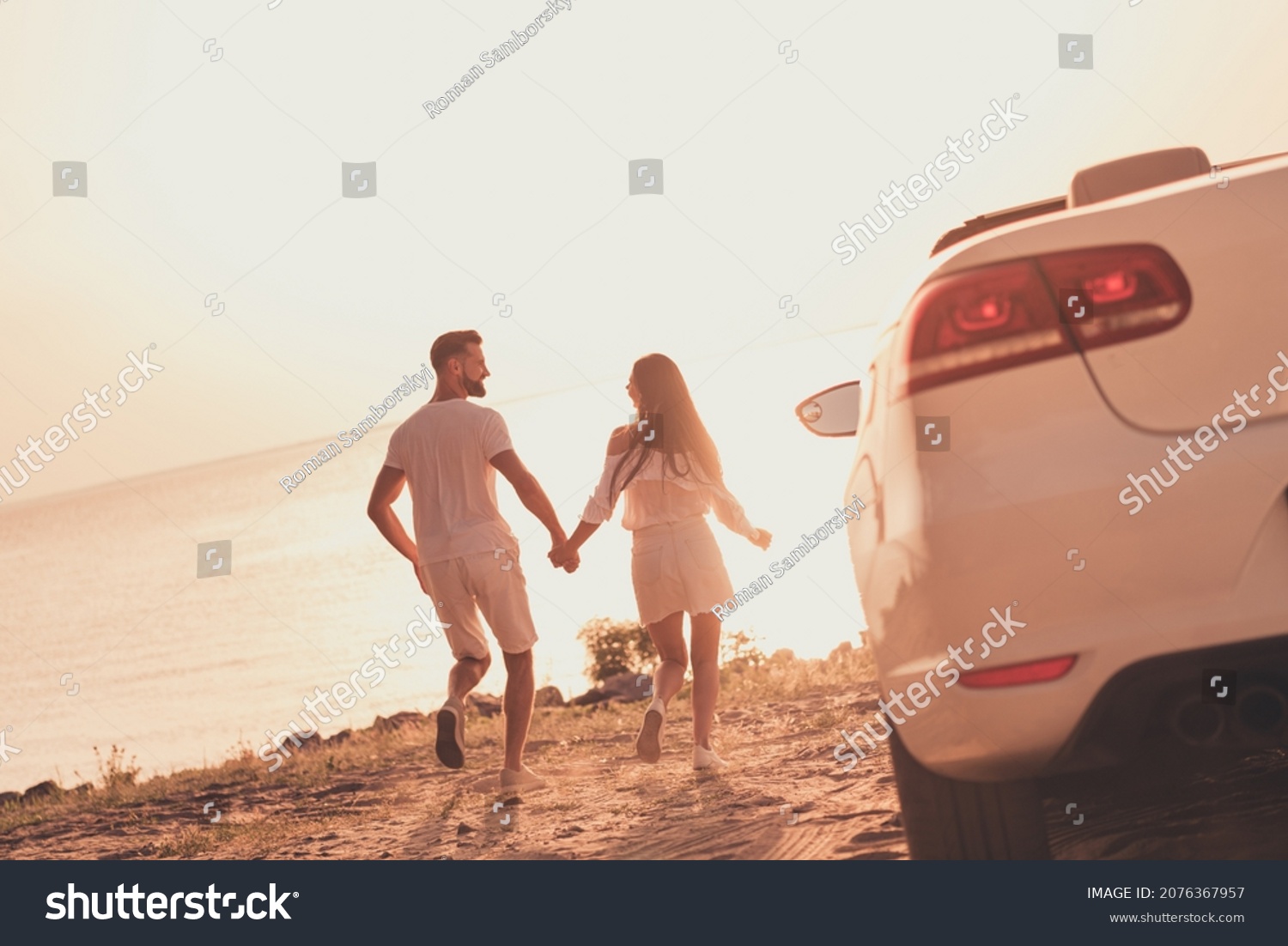Photo of cheerful carefree married couple dressed white clothes driving car walking beach holding arms outdoors country side road #2076367957