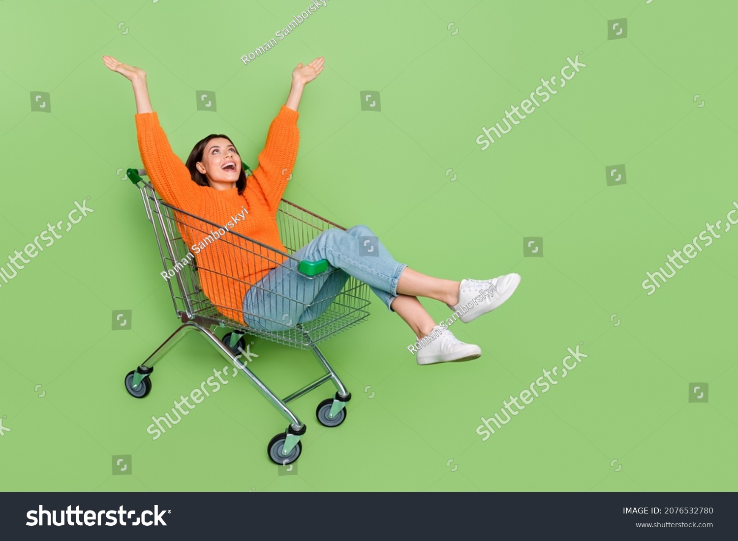 Full length photo of crazy lady ride push cart raise arms up amazed autumn bargain isolated over green color background #2076532780