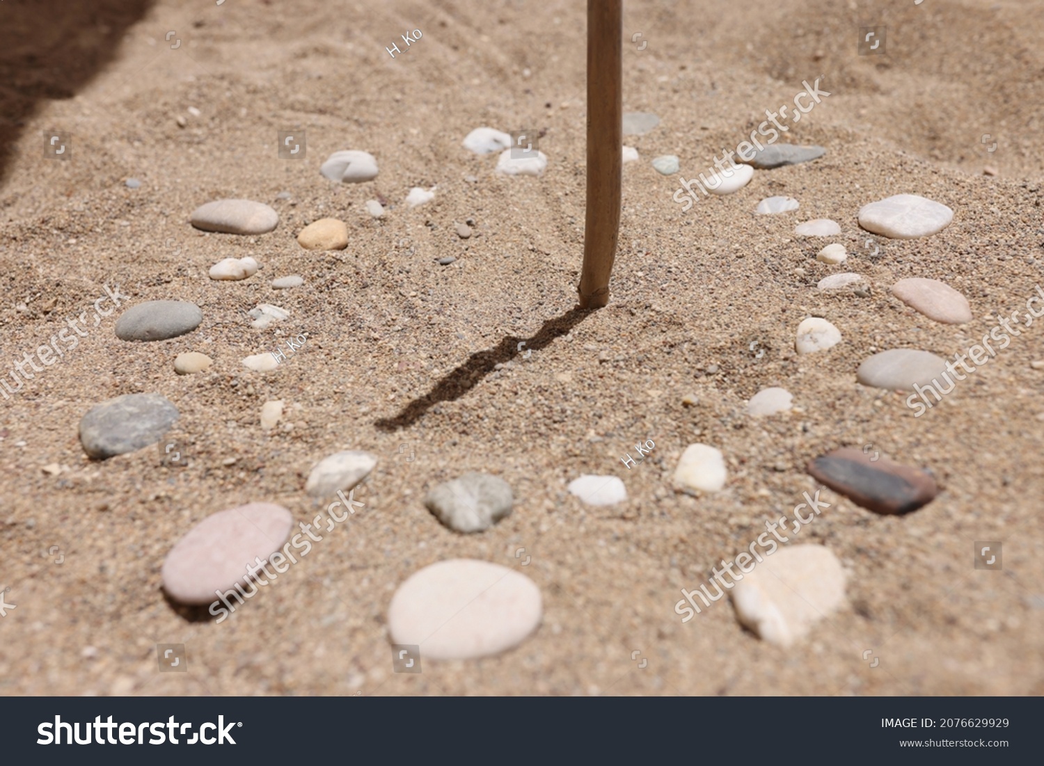 Wooden stick and pebbles on sand showing time by shadow #2076629929