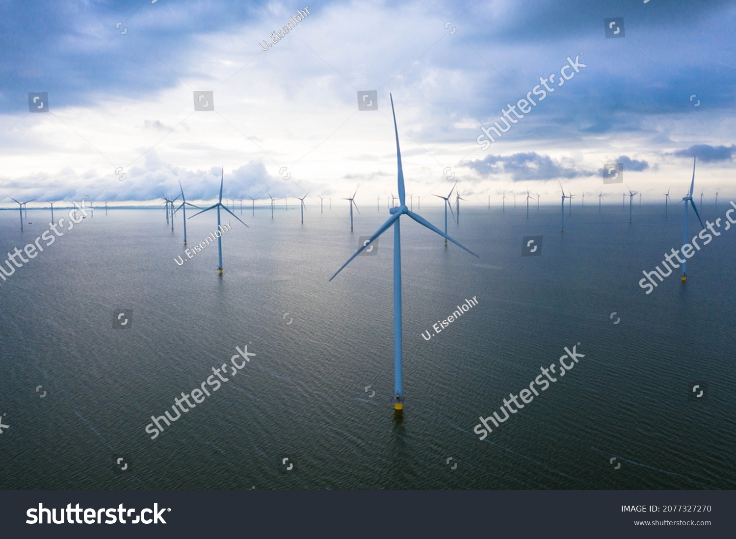 Aerial view of enormous windmills stand in the sea along a dutch sea. Fryslân wind farm, the largest inland wind farm in the world. Friesland, Afsluitdiijk, Ijsselmeer, Breezanddijk, Netherlands #2077327270