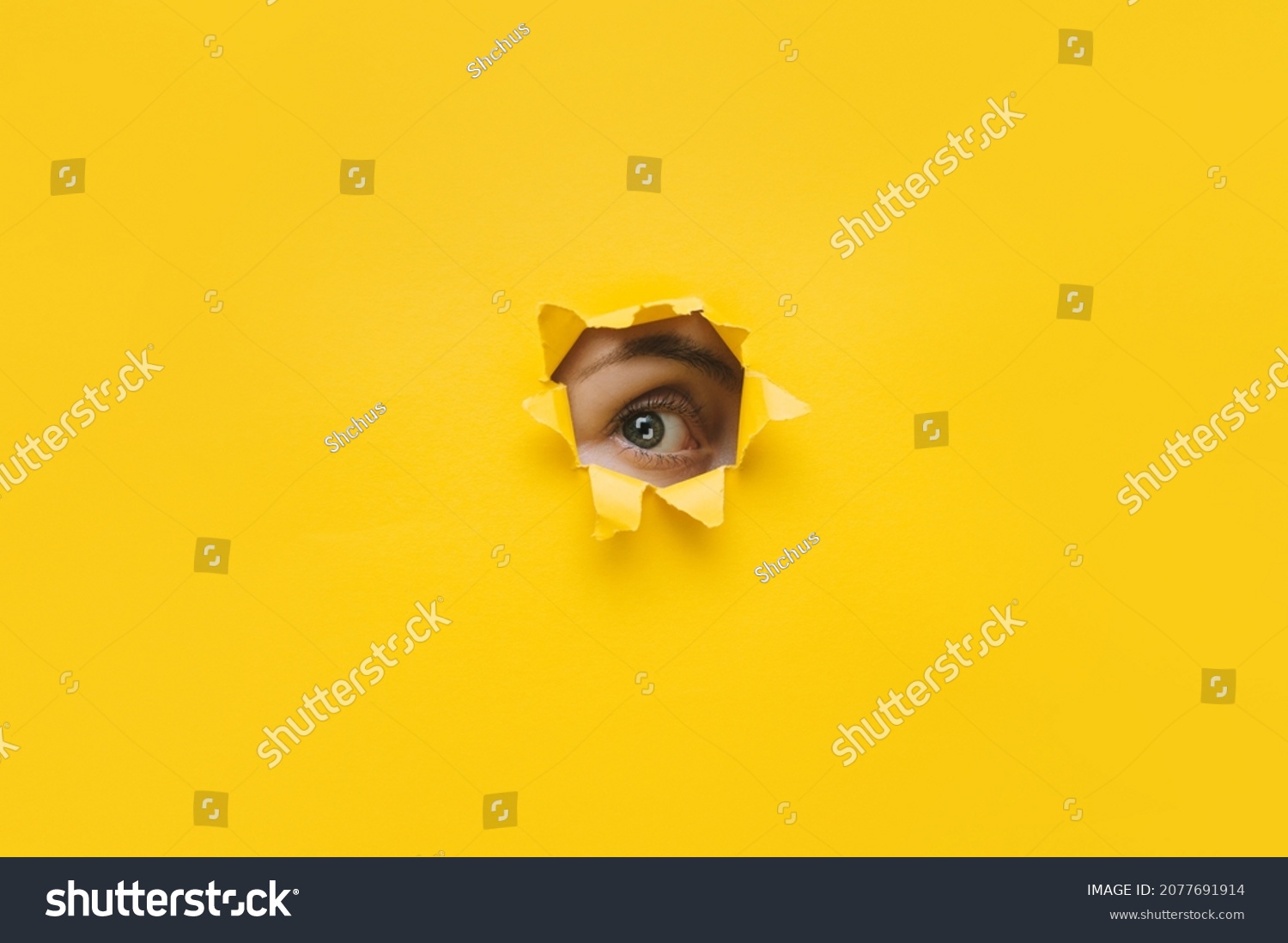 One eye looking through a hole in a yellow paper. Voyeurism. Woman is watching the husband. A curious look. Jealousy, spying on or overhearing the concept. Copy space. #2077691914