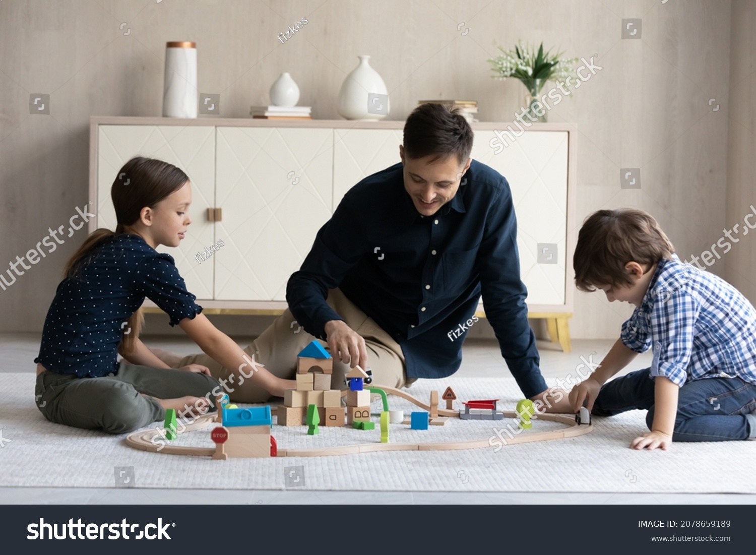 Father and children play toy railroad, loving family sit on warm floor in modern living room enjoy wooden plaything and playtime together. Weekend leisure and fun, quarantine with kids at home concept #2078659189