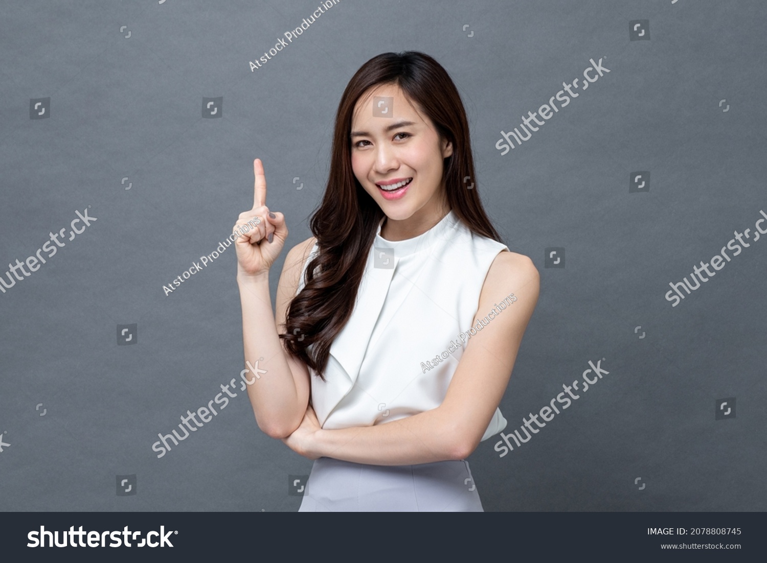 Smiling beautiful Asian woman pointing finger upward to empty space in studio gray isolated background #2078808745
