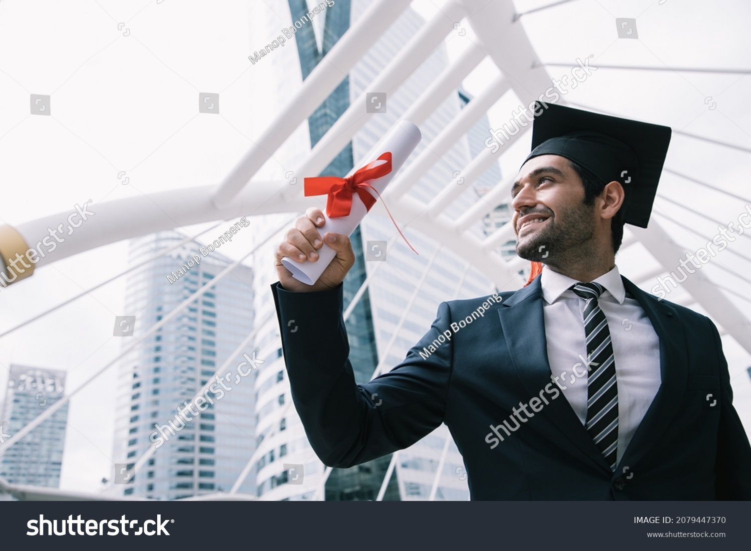 Handsome businessman wear graduation degree hat and stand on stair near cityscape, business education concept #2079447370