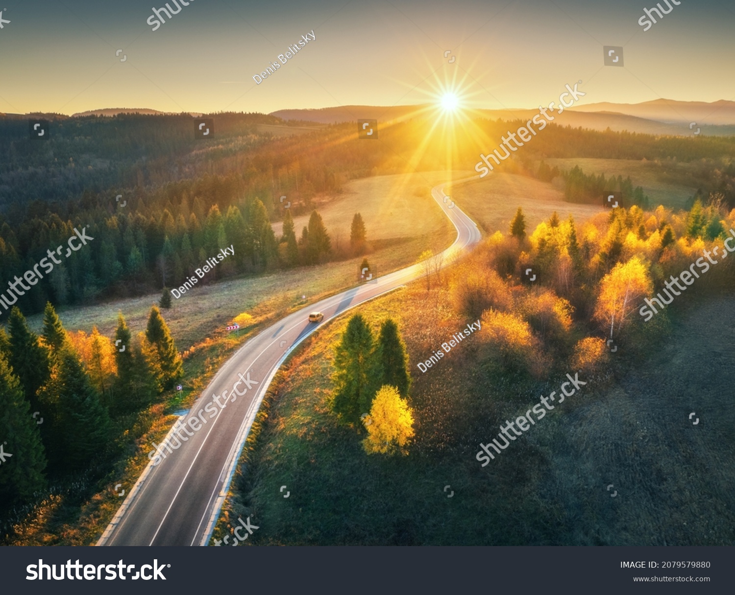 Aerial view of mountain road in forest at sunset in autumn. Top view from drone of road in woods. Beautiful landscape with roadway in hills, pine trees, green meadows, golden sunlight in fall. Travel #2079579880